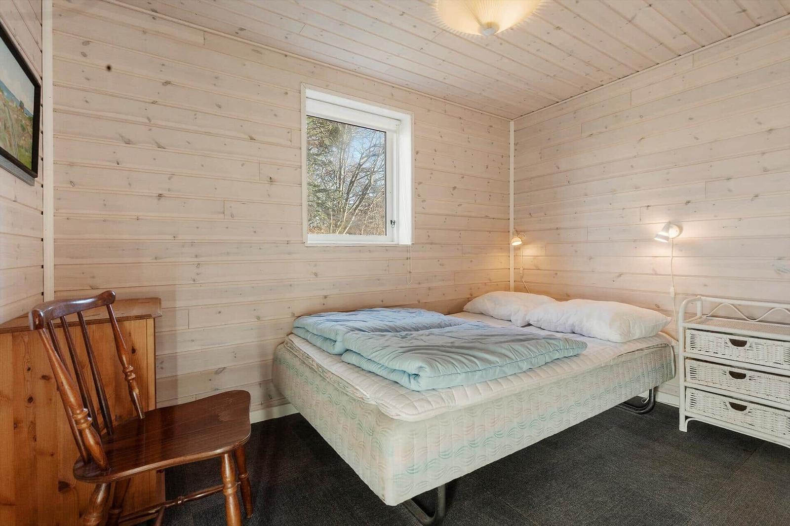 Bedroom with bed, chair, and window. Wooden walls and white furniture.