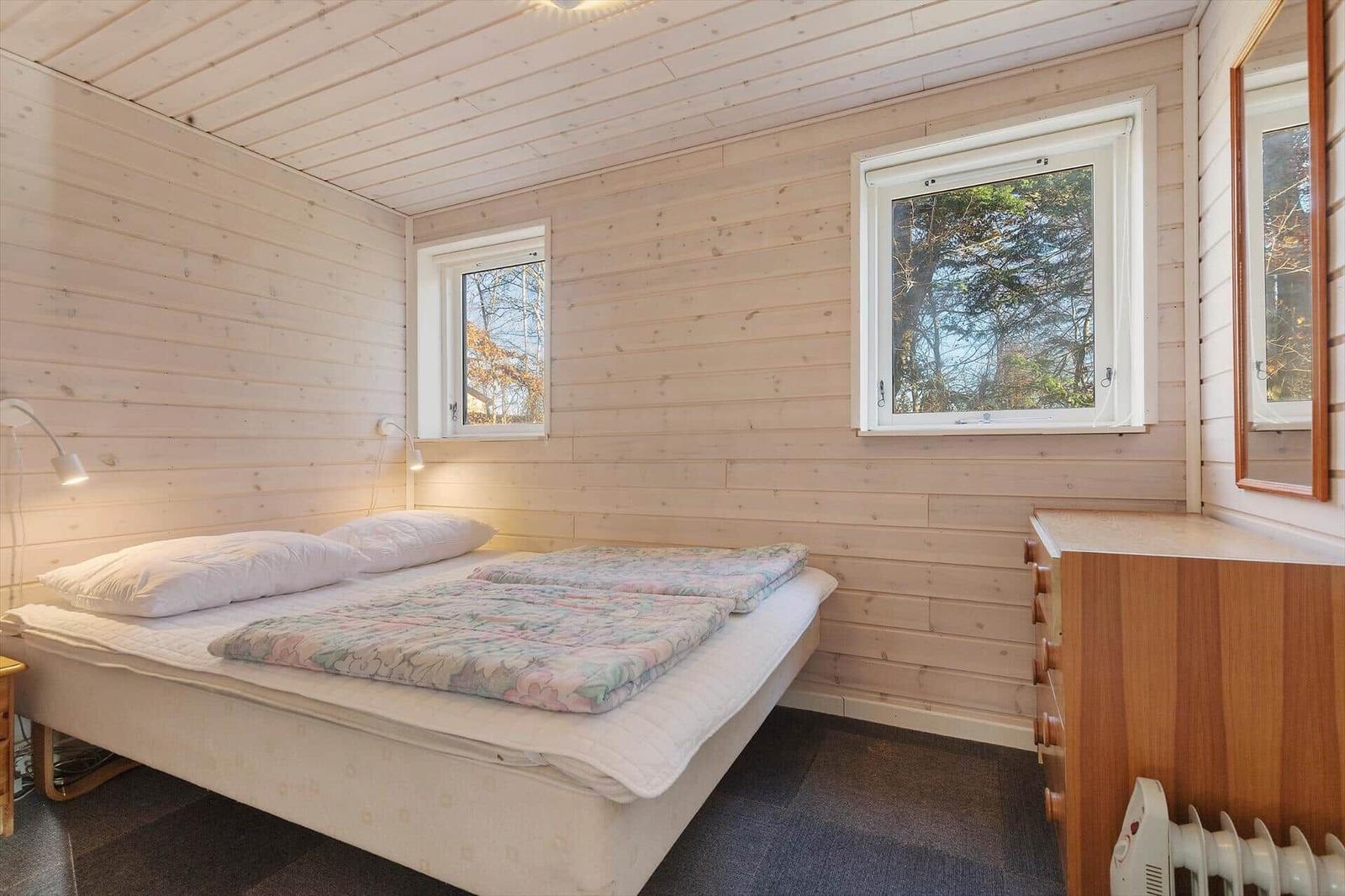 Bedroom with bed, two windows, and wood paneling.