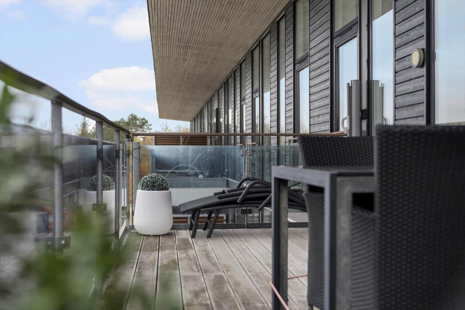 Terrasse mit Loungemöbeln, Glasgeländer und Pflanzen. Modernes Haus mit Holzfassade.