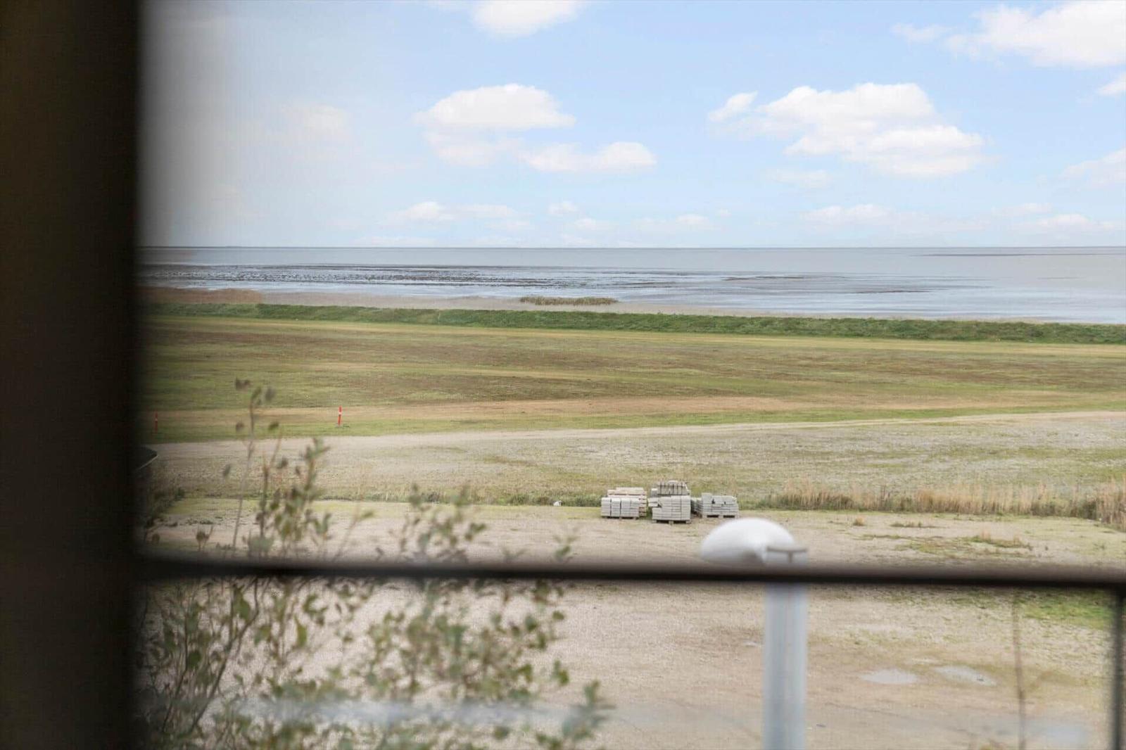 Blick vom Fenster auf Flachland und Wasser unter blauem Himmel mit weißen Wolken.
