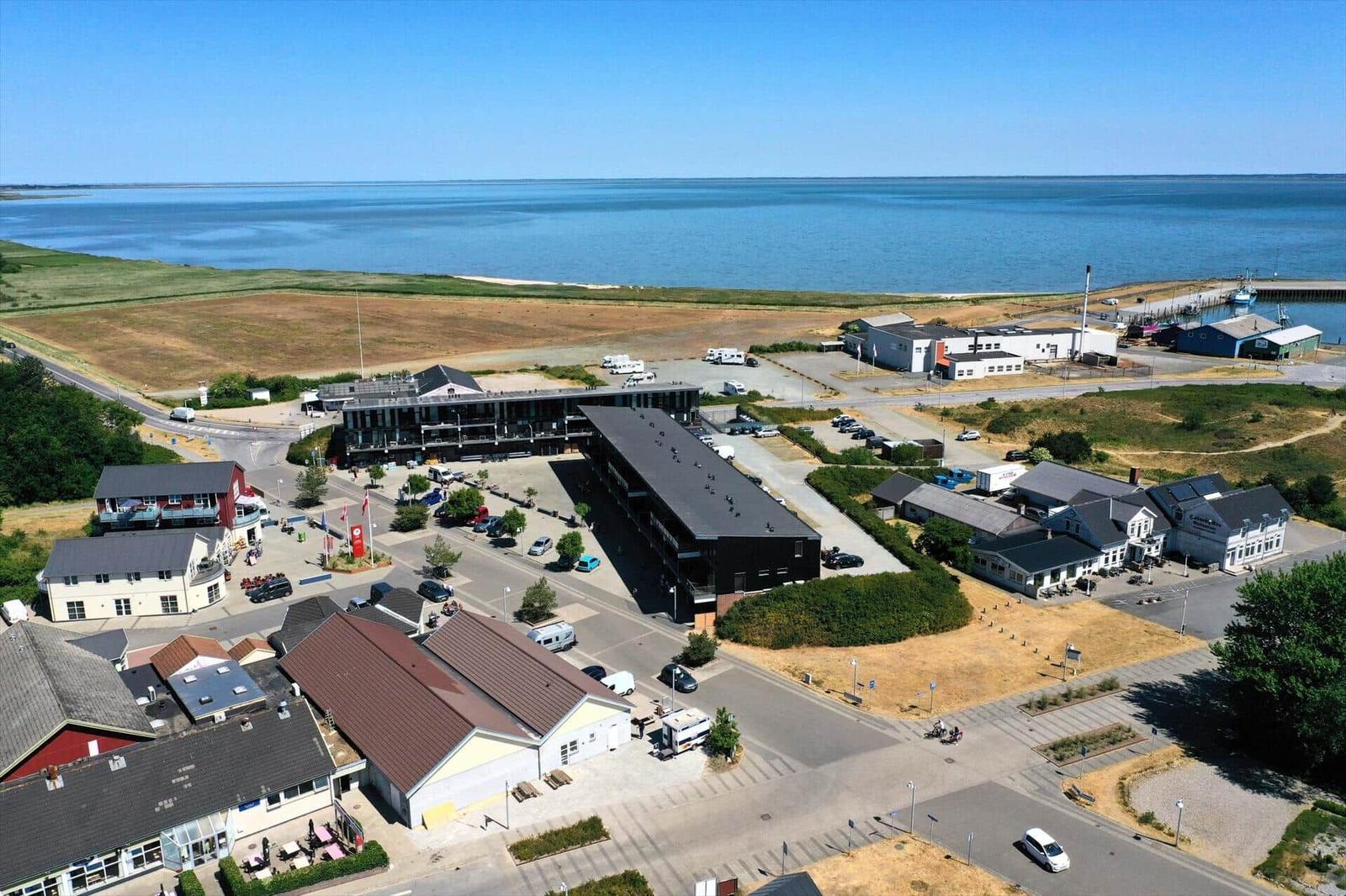 Aerial view of a coastal village with buildings, parking, and a large body of water.