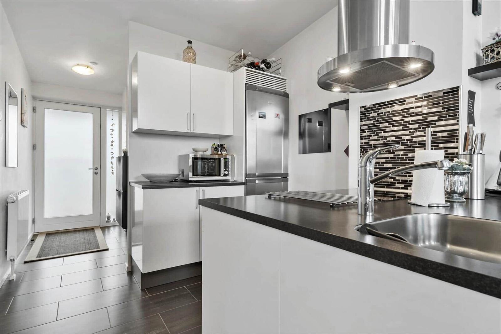 Moderne Küche mit Edelstahlspüle, Kücheninsel und Kühlschrank.