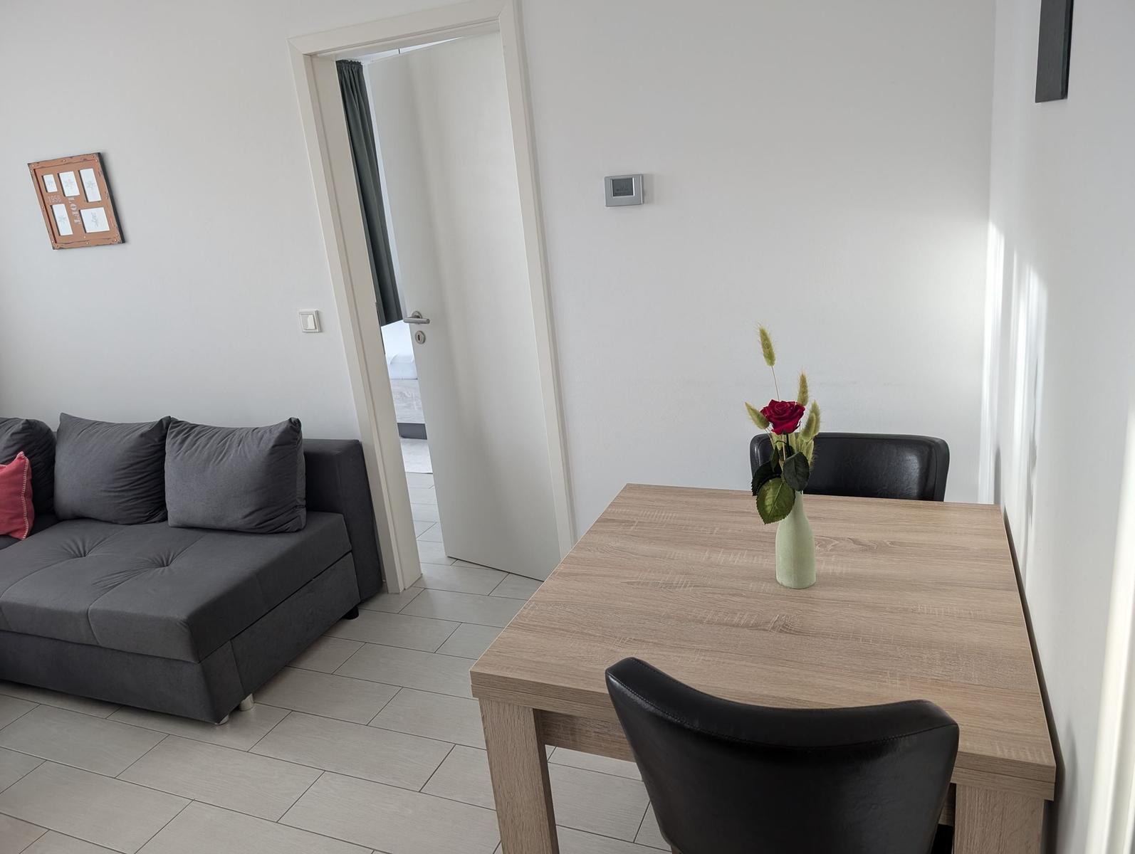 Essbereich mit Tisch und Stühlen, daneben Wohnbereich mit Sofa und Tür zum Schlafzimmer.