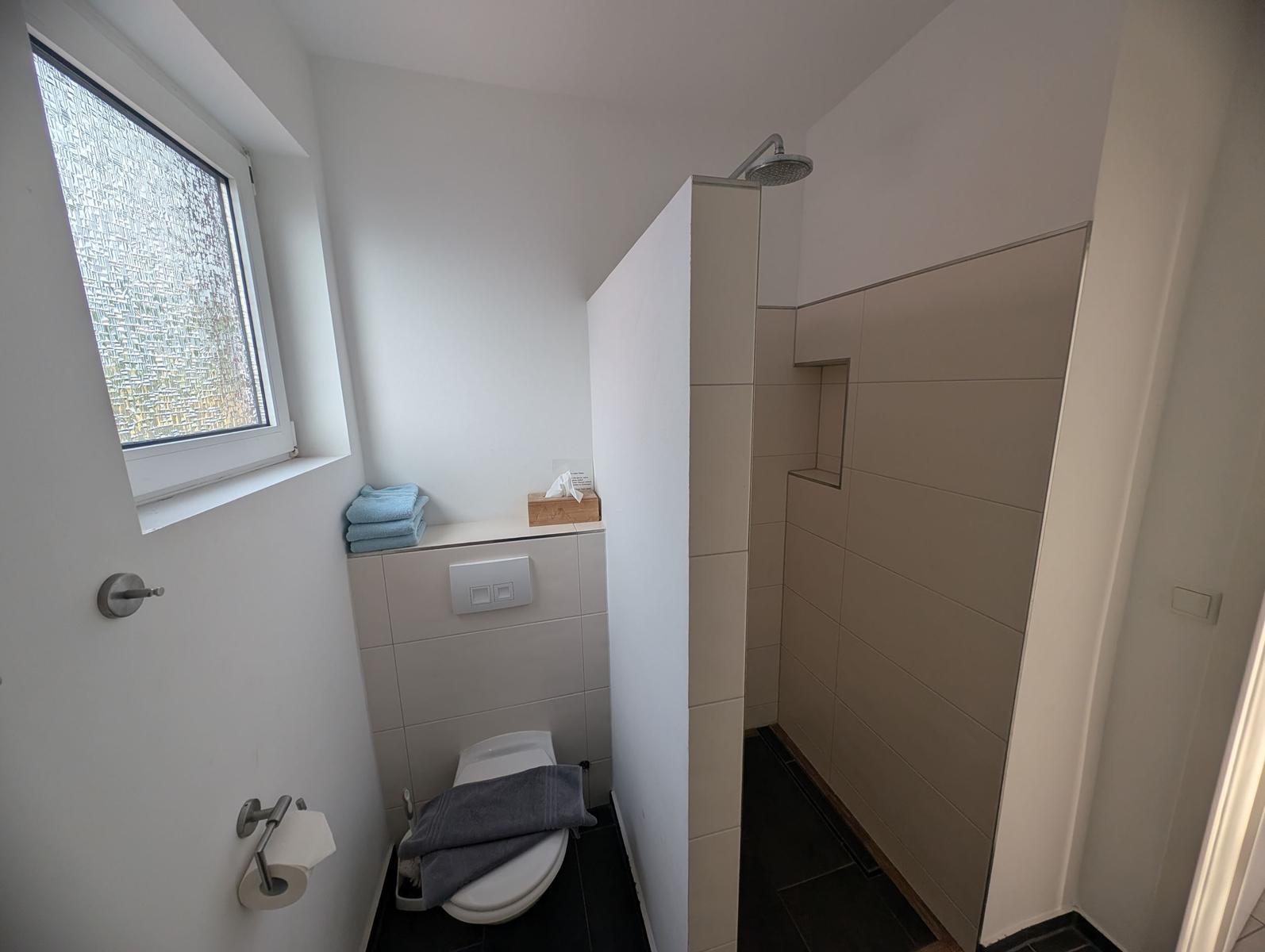 Badezimmer mit Dusche, Toilette und Fenster