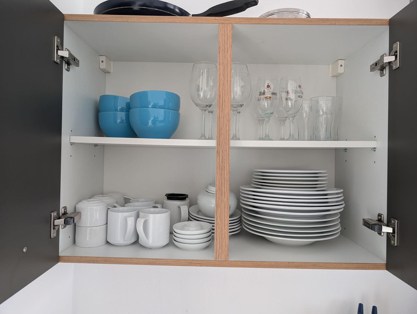 Küchenschrank mit Tassen, Tellern, Gläsern und blauen Schüsseln.