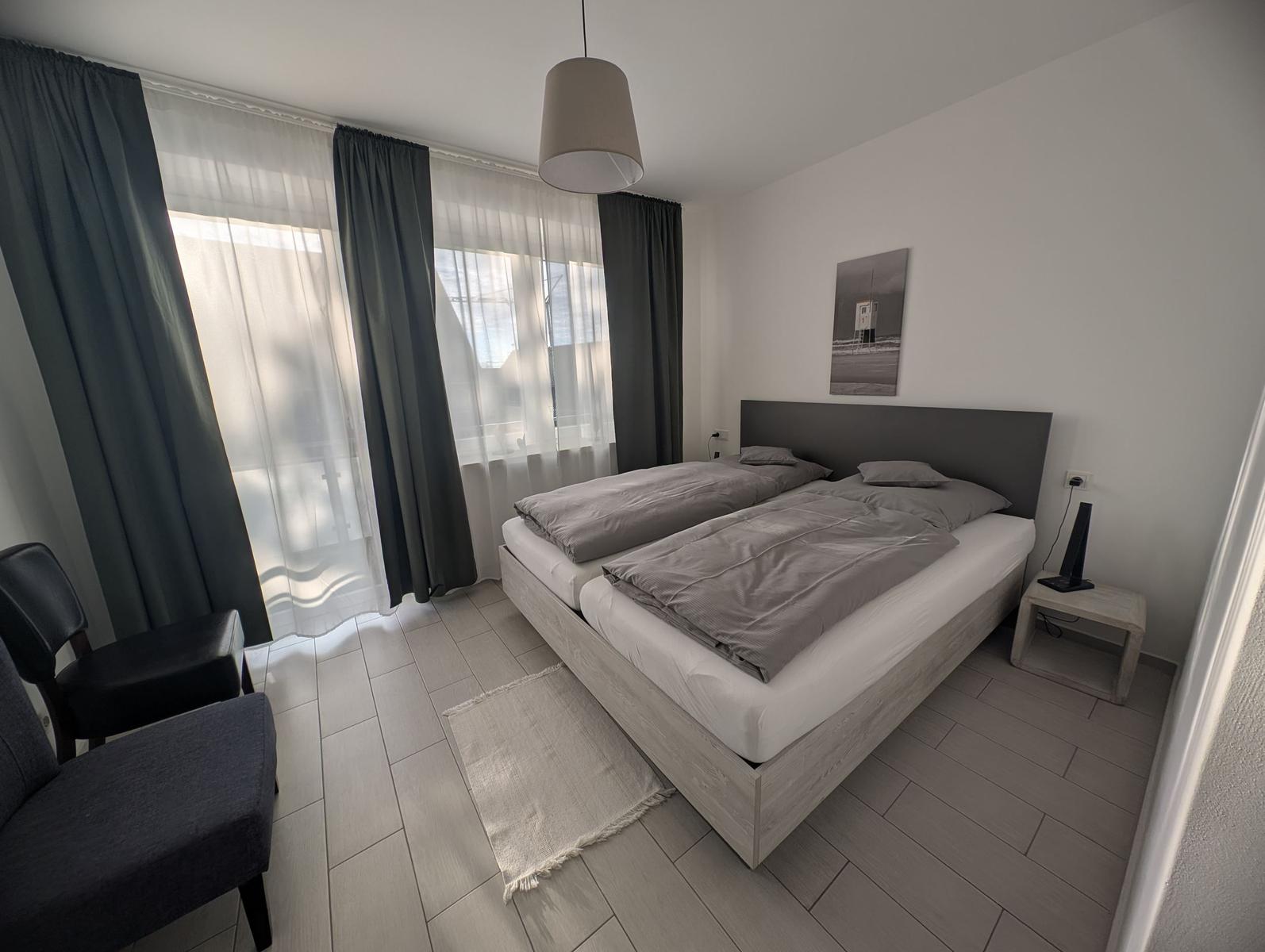 Schlafzimmer mit Doppelbett, Fenster und Sitzgelegenheit.