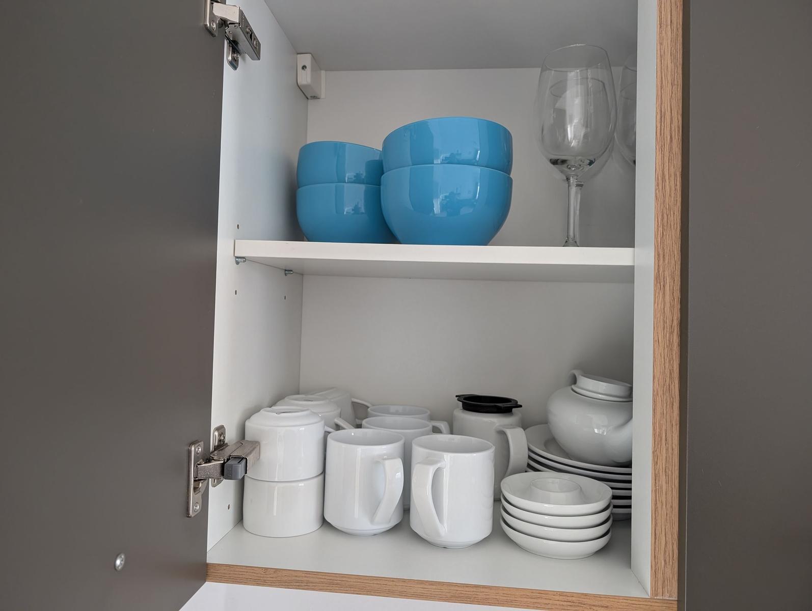 Schrank mit blauen Schüsseln, Weingläsern und weißer Tasse, Teller und Teekanne.