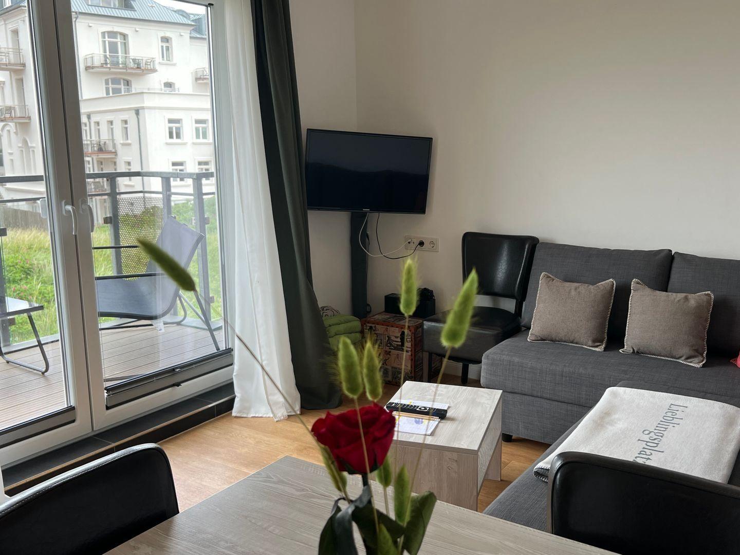 Wohnbereich mit Sofa, Fernseher und Balkonansicht.
