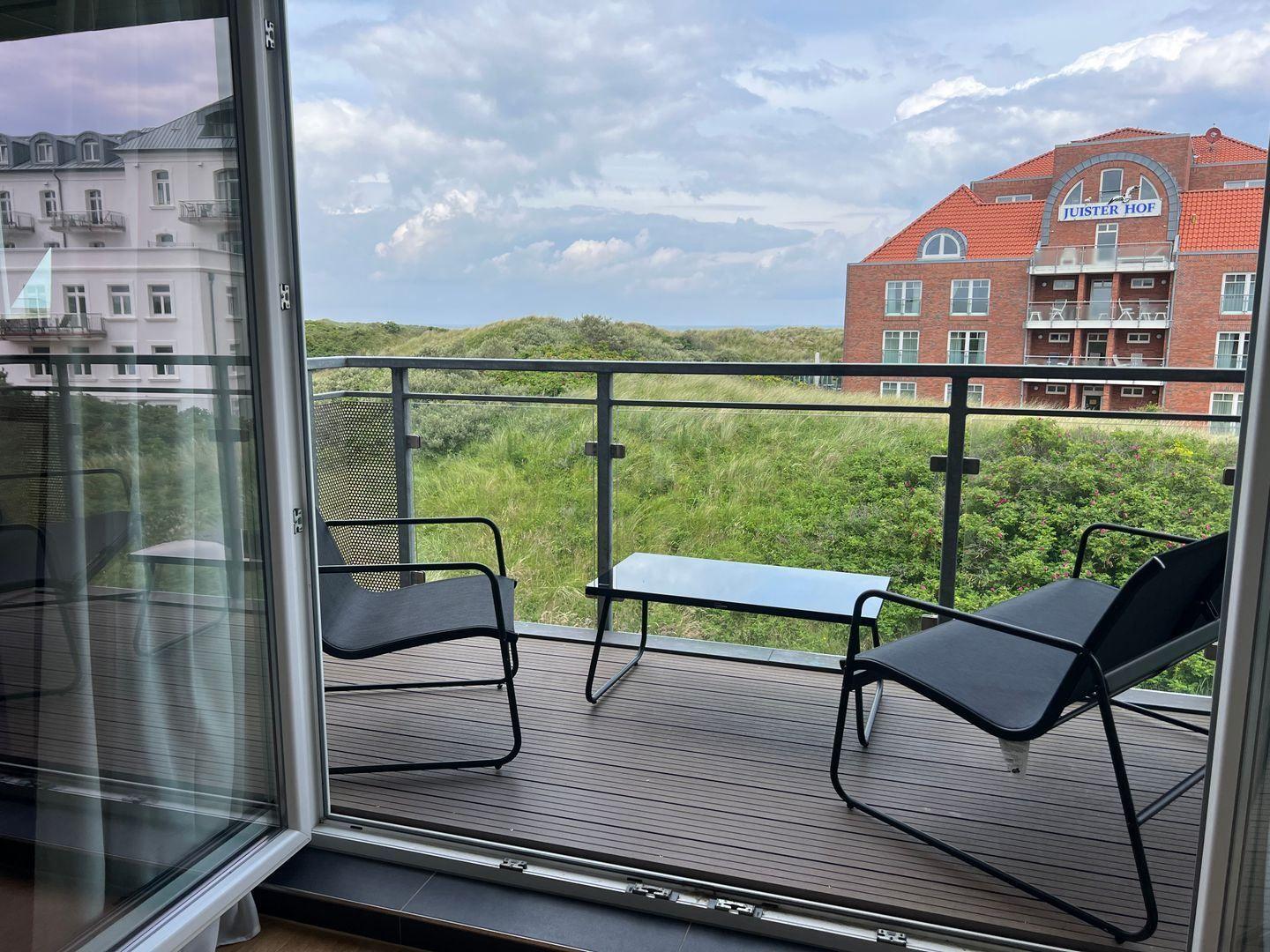 Terrasse mit zwei Stühlen und Tisch. Blick auf Grünflächen und Gebäude.