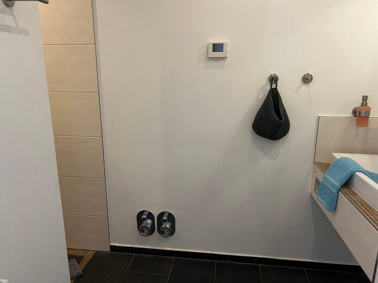 Badezimmer mit Dusche, Waschbecken und Wandthermostat.