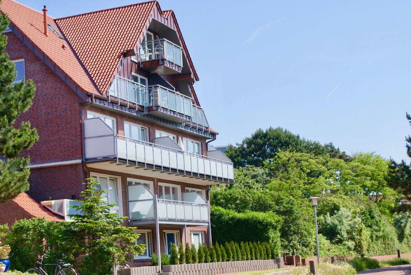 Zweistöckiges Haus mit Balkonen und rotem Dach, umgeben von Bäumen und Grünflächen.