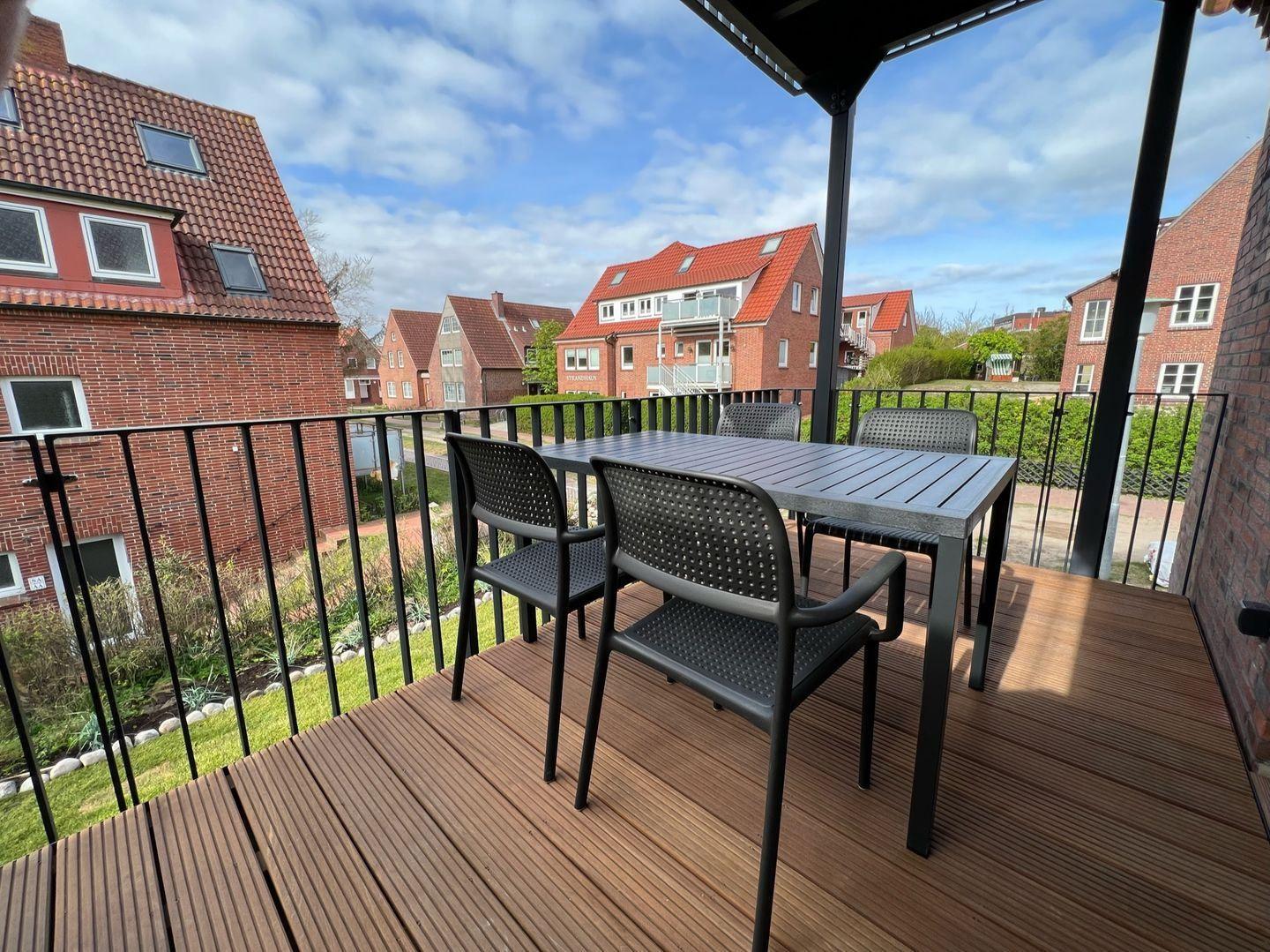 Terrasse mit Tisch und Stühlen, Blick auf Wohnhäuser und Garten.
