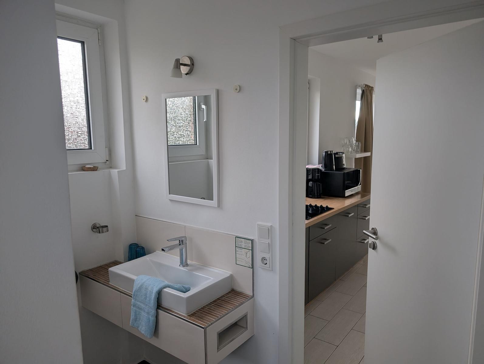 Badezimmer mit Waschbecken und Spiegel. Küche mit Arbeitsplatte und Geräten.