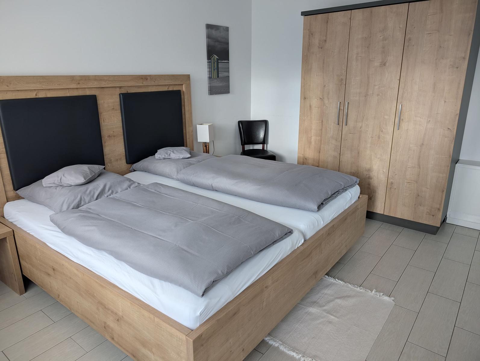 Doppelbett mit grauer Bettwäsche, Kleiderschrank und Stuhl im Schlafzimmer.