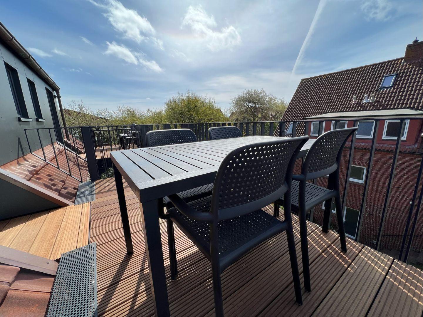 Terrasse mit Tisch und Stühlen, Blick auf Wohnhäuser und Bäume.