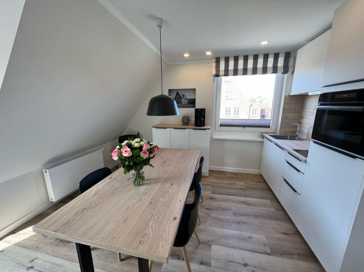 Essbereich mit Tisch, Stühlen und Blumen. Küche mit Arbeitsplatte und Fenster.