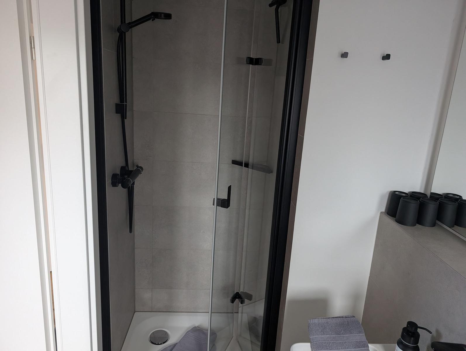 Duschkabine mit Glaswand und schwarzen Armaturen. Handtuch und Pflegeprodukte sind vorhanden.