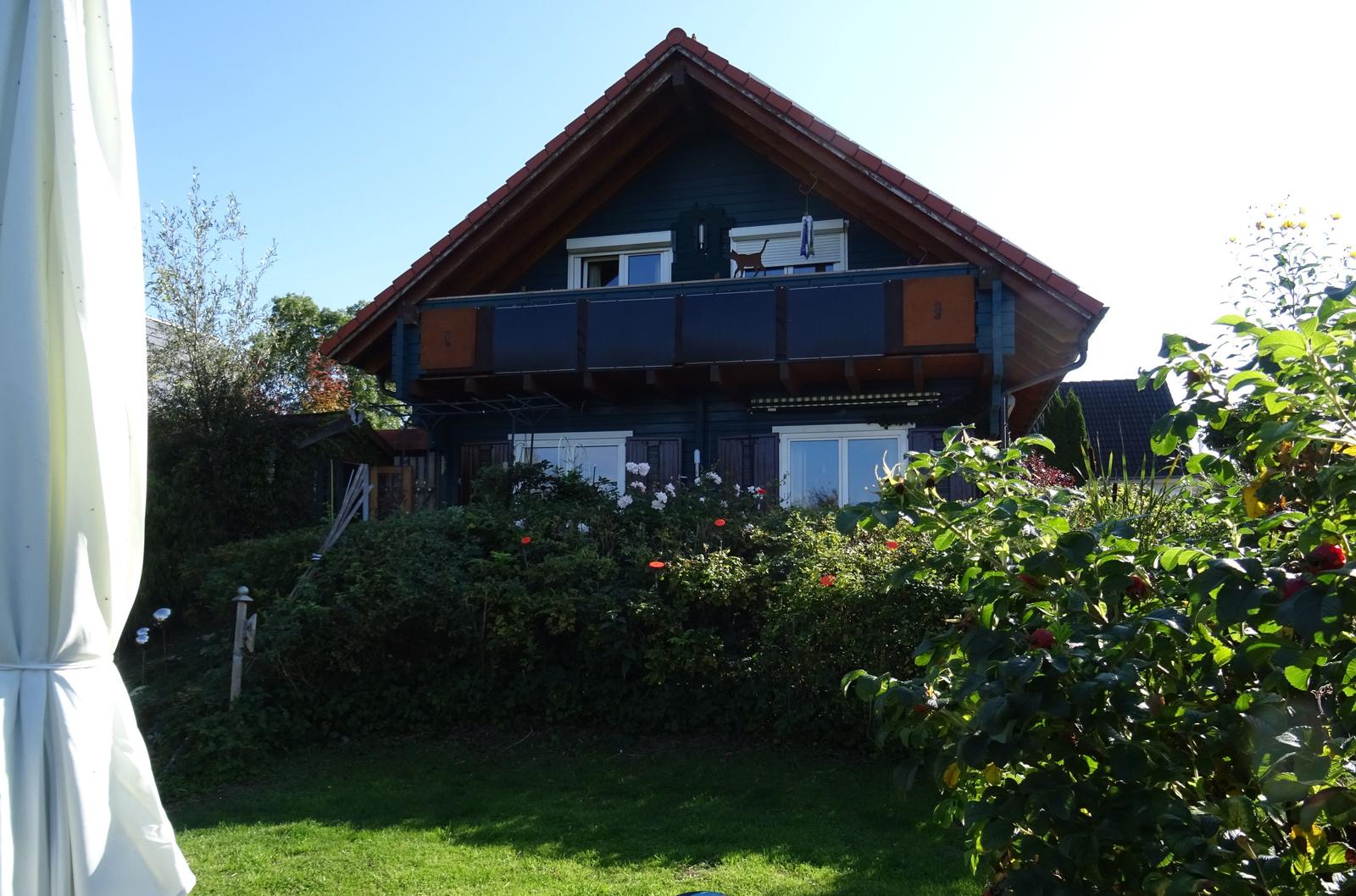 Haus mit Balkon, Garten und Blumen. Sonniger Tag.