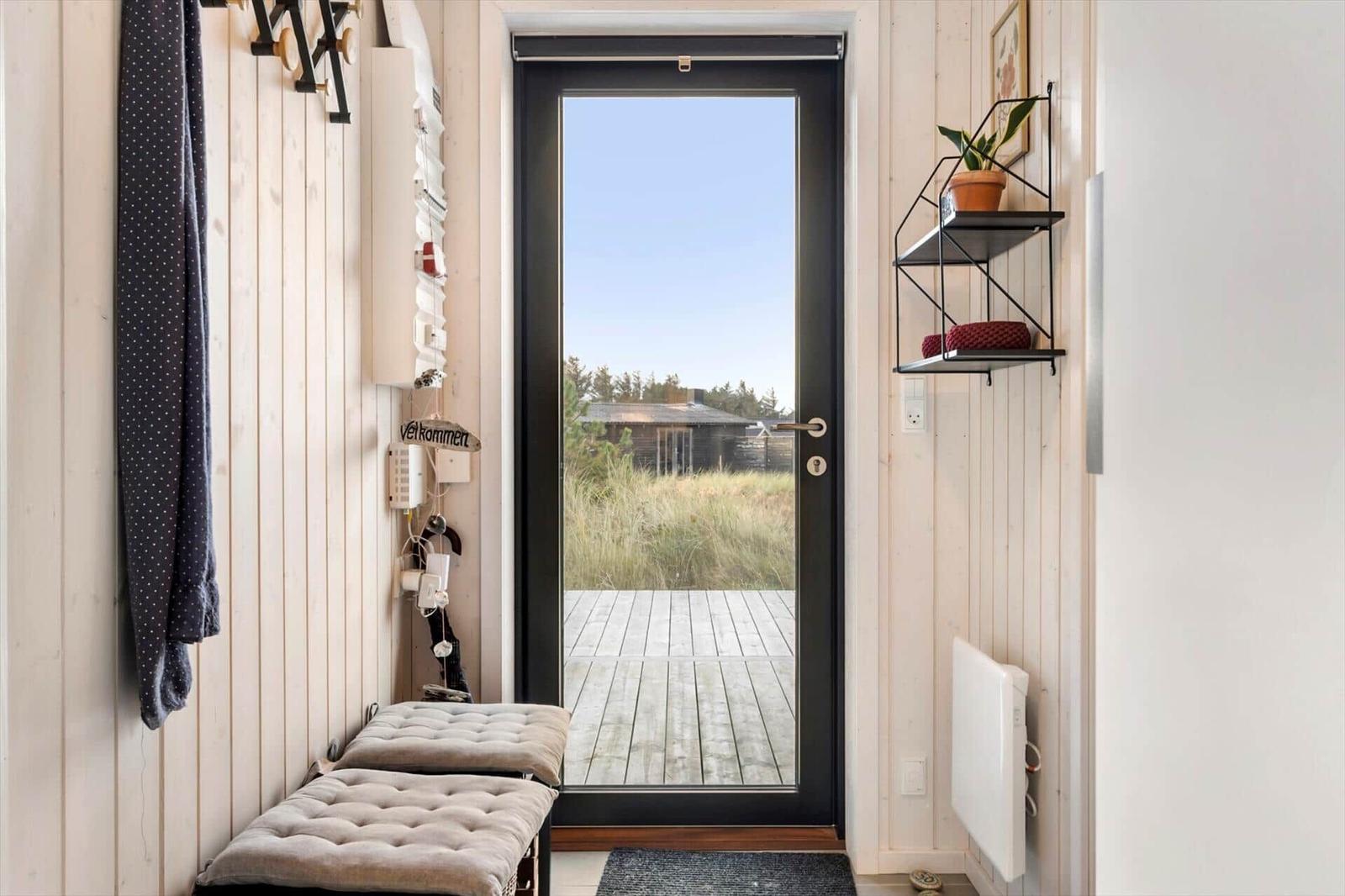 Entrance with door to wooden terrace and green area. Wall shelves and bench.