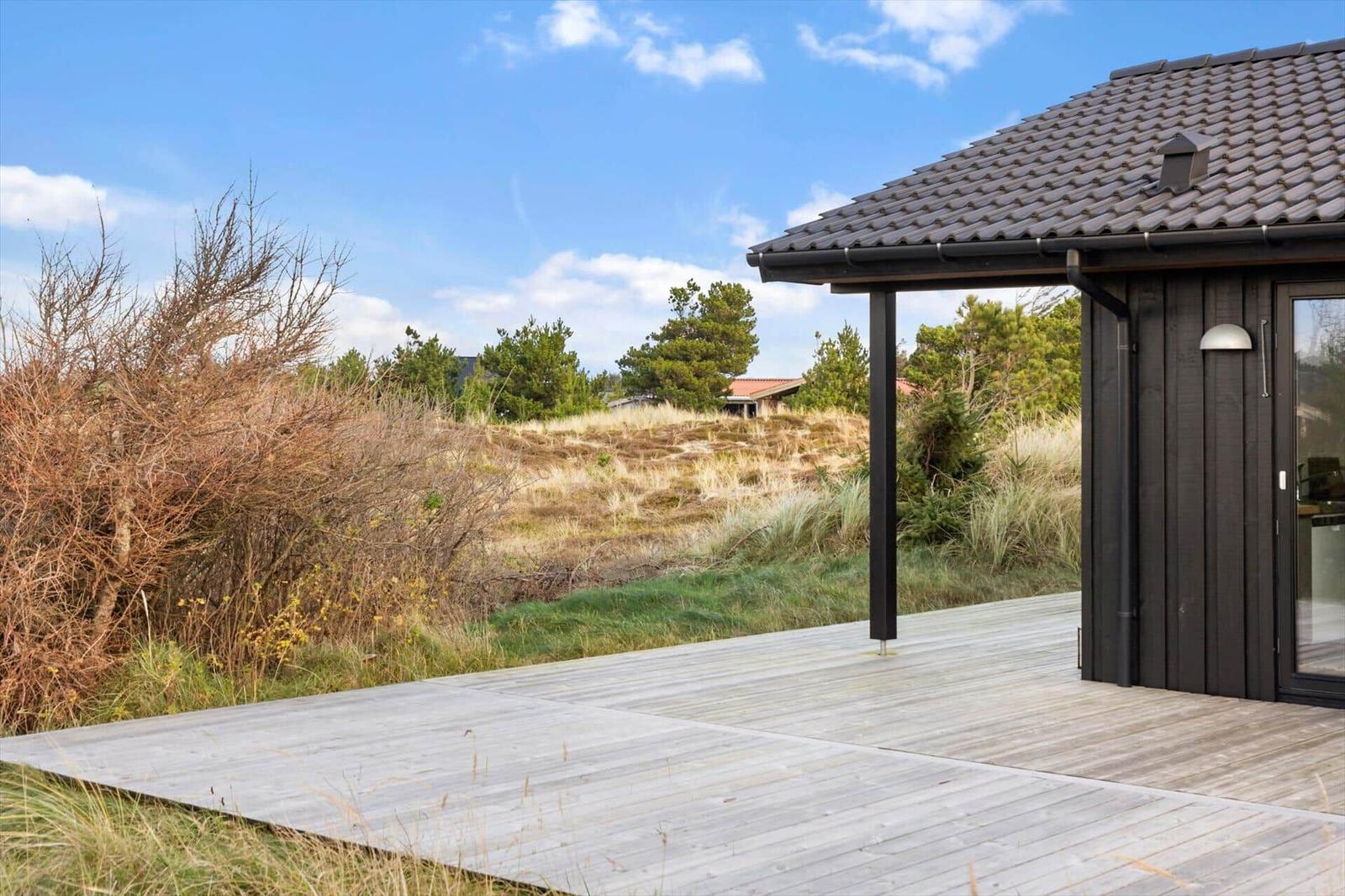 Wooden terrace with view of grassland and trees under blue sky.