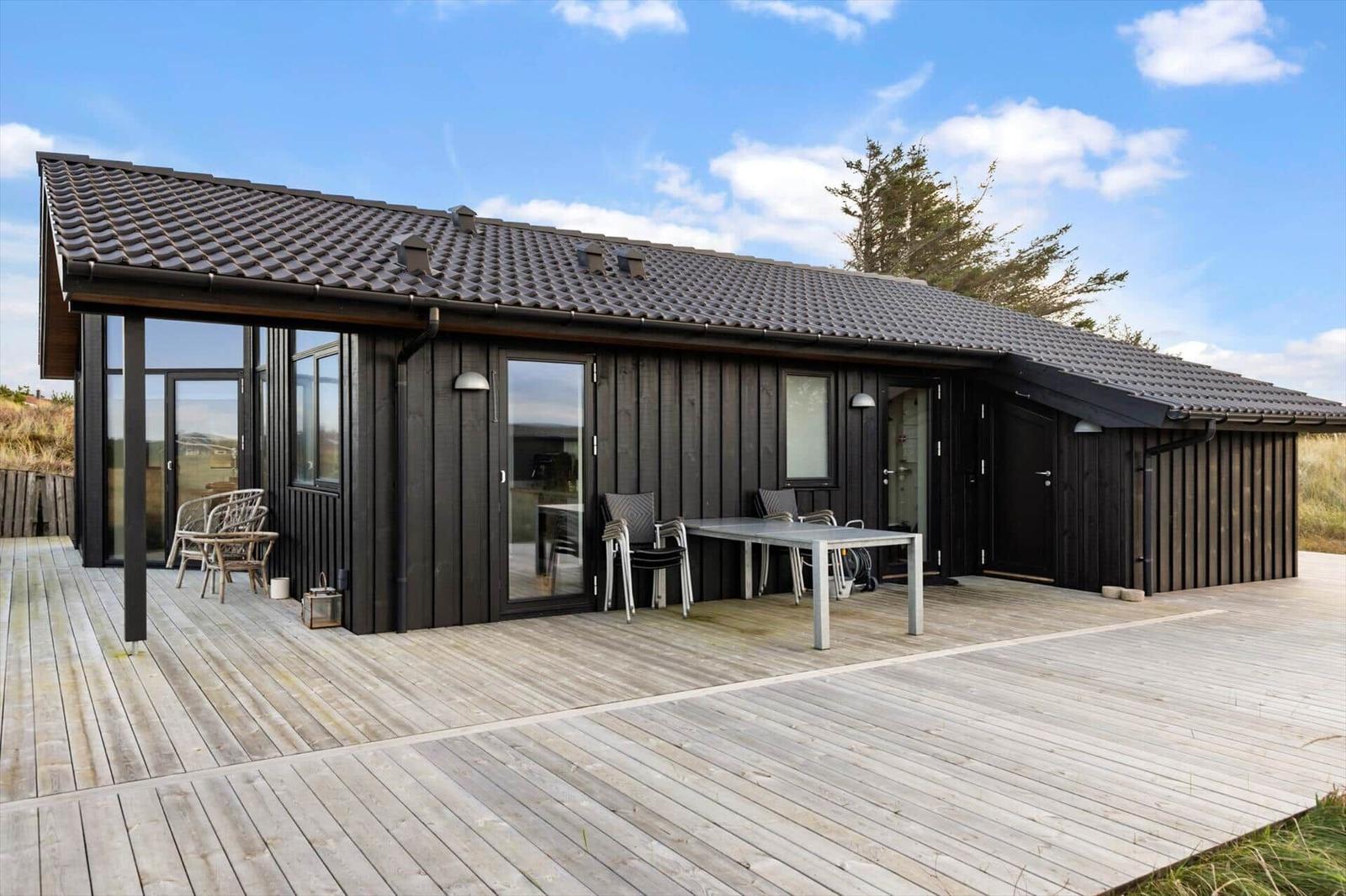 Modern wooden cabin with terrace, table, and chairs. Background: sky and trees.