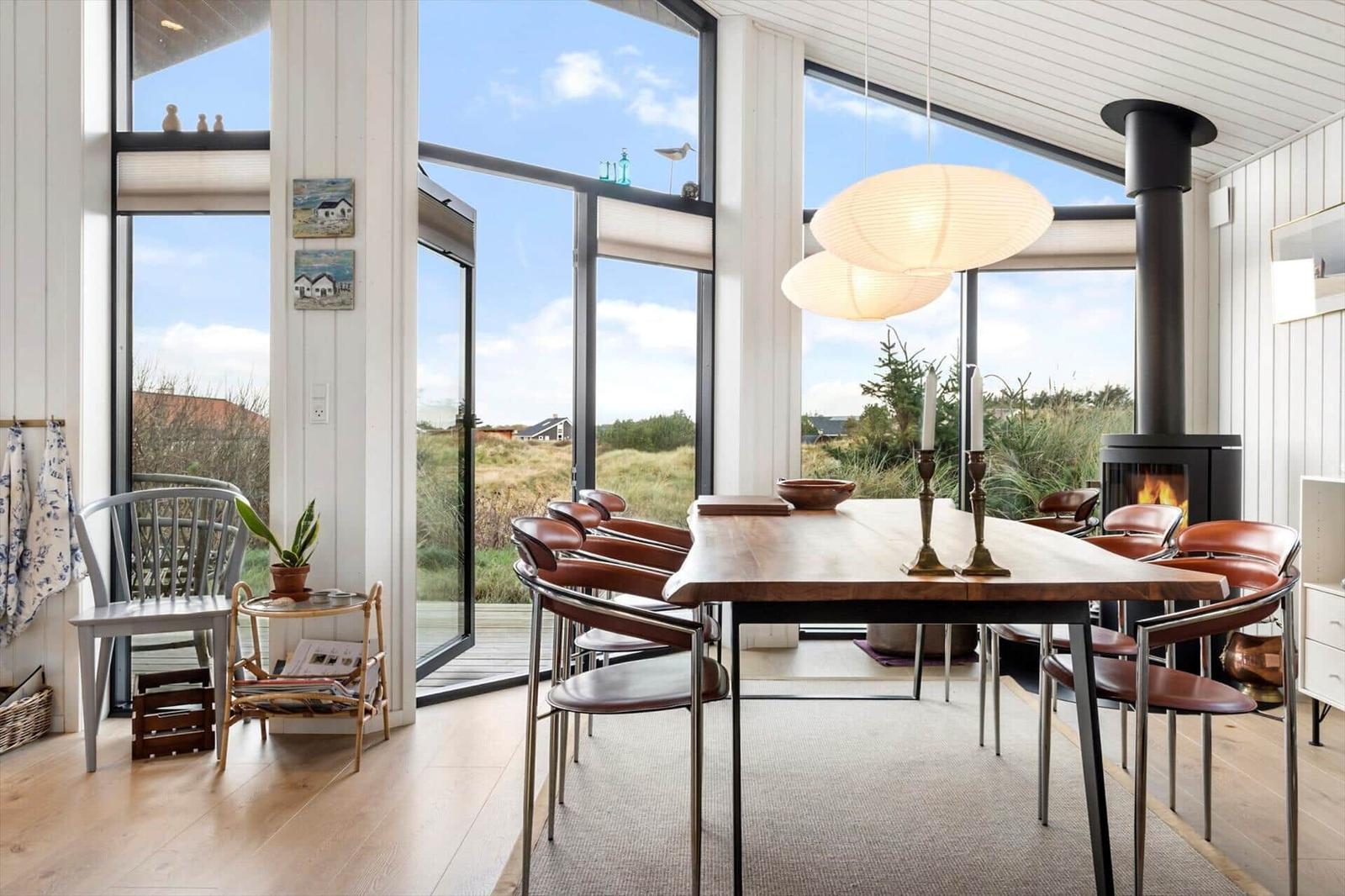 Dining room with wooden table, leather chairs, and fireplace. Large windows overlook grassland.