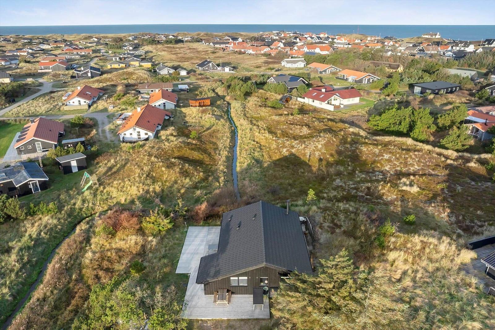 House with terrace in dunes, view of coastal village and sea.