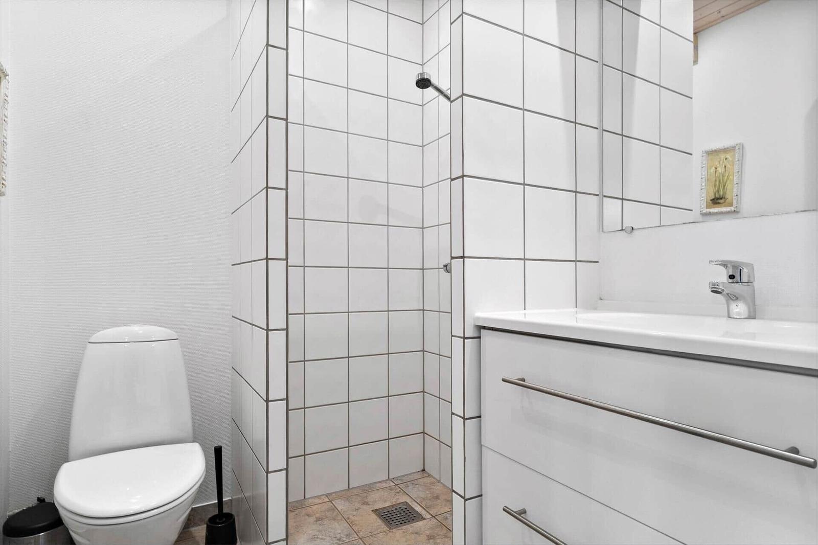 Bathroom with shower, sink and toilet. White tiles and mirror.
