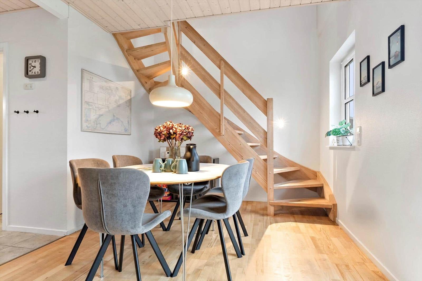 Dining area with table, chairs, and wooden staircase.