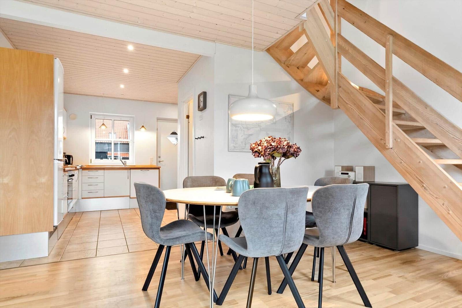 Dining area with table and chairs, kitchen and wooden staircase