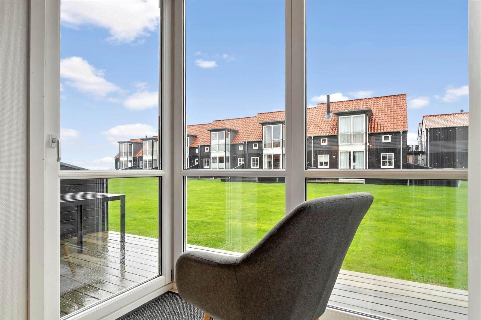 A gray chair sits by a large window overlooking a green lawn and modern houses.