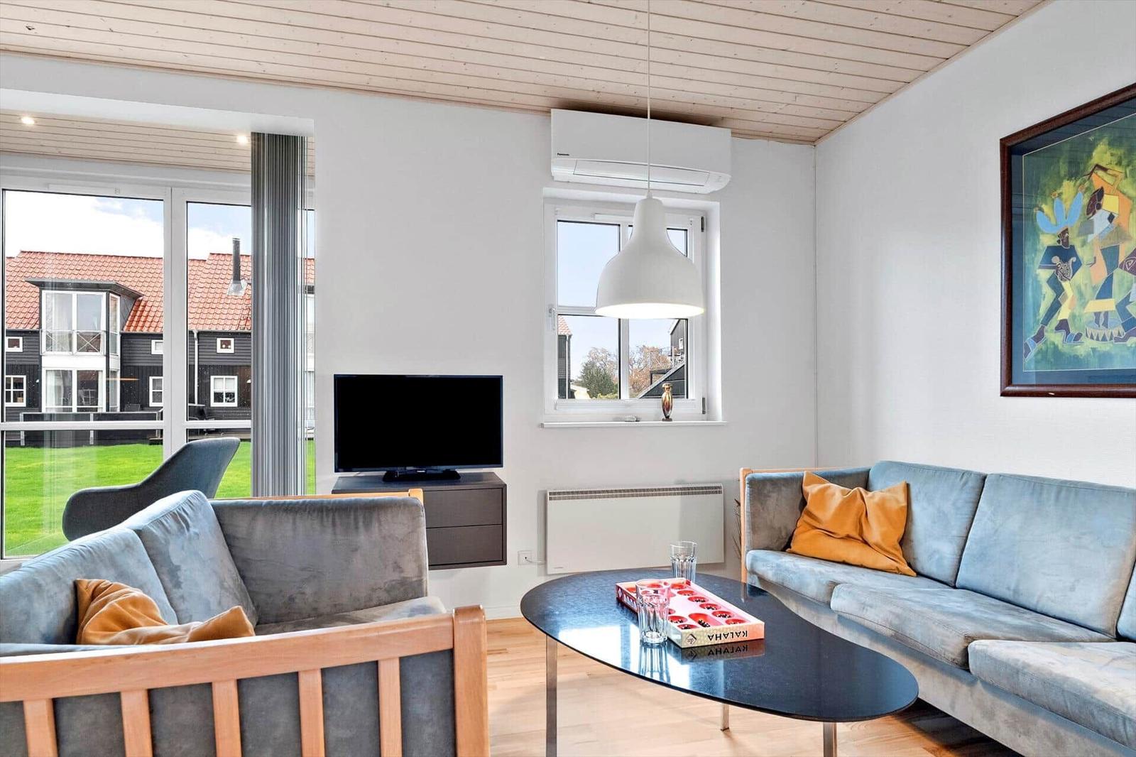 Living room with sofa, coffee table, and TV. Large windows and wooden ceiling.