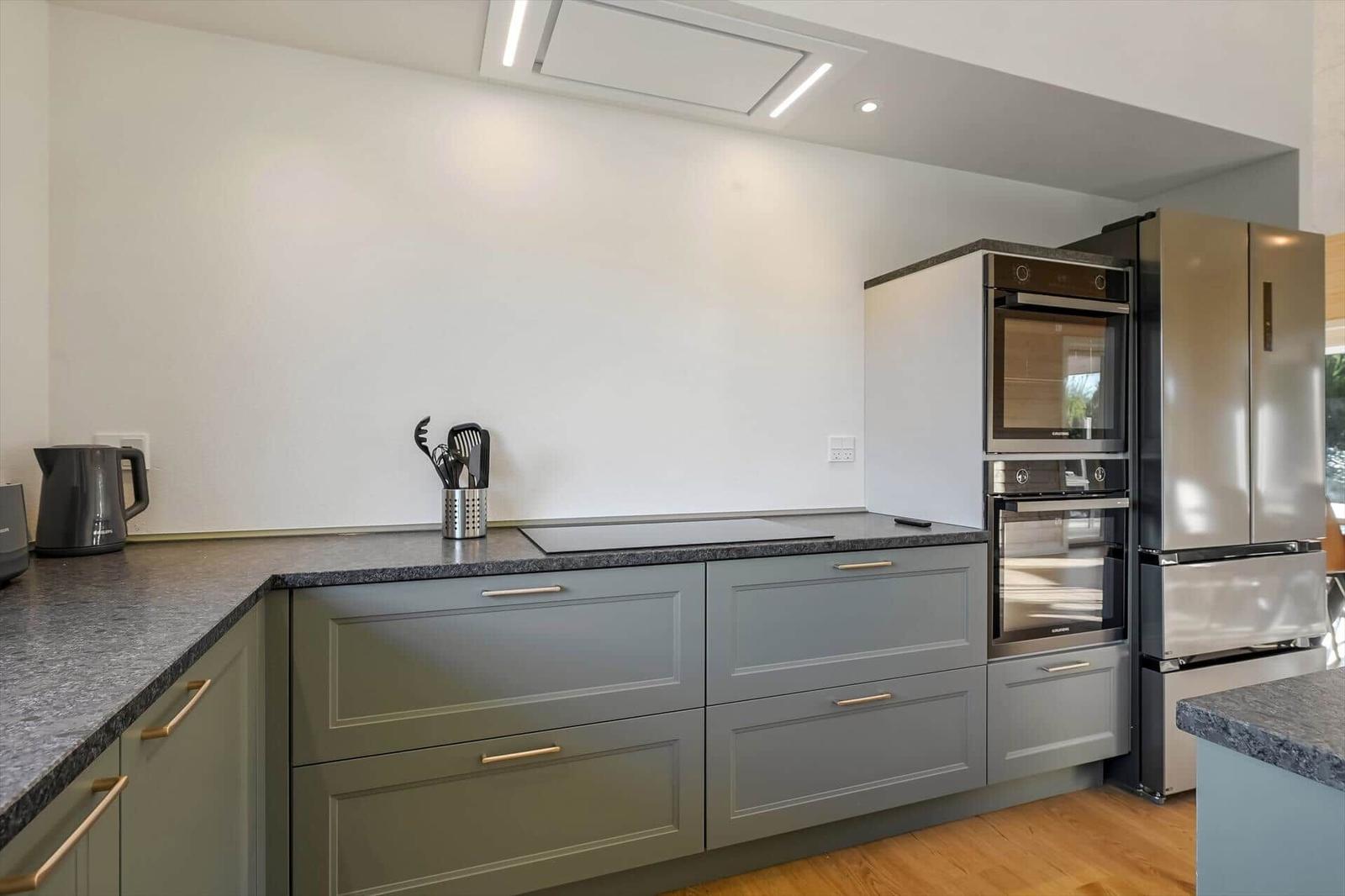 Modern kitchen with gray cabinets, stainless steel appliances, and dark countertop.