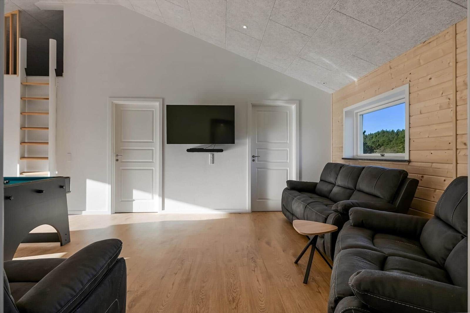Living room with sofa, TV, and pool table. Wood wall and window with view.