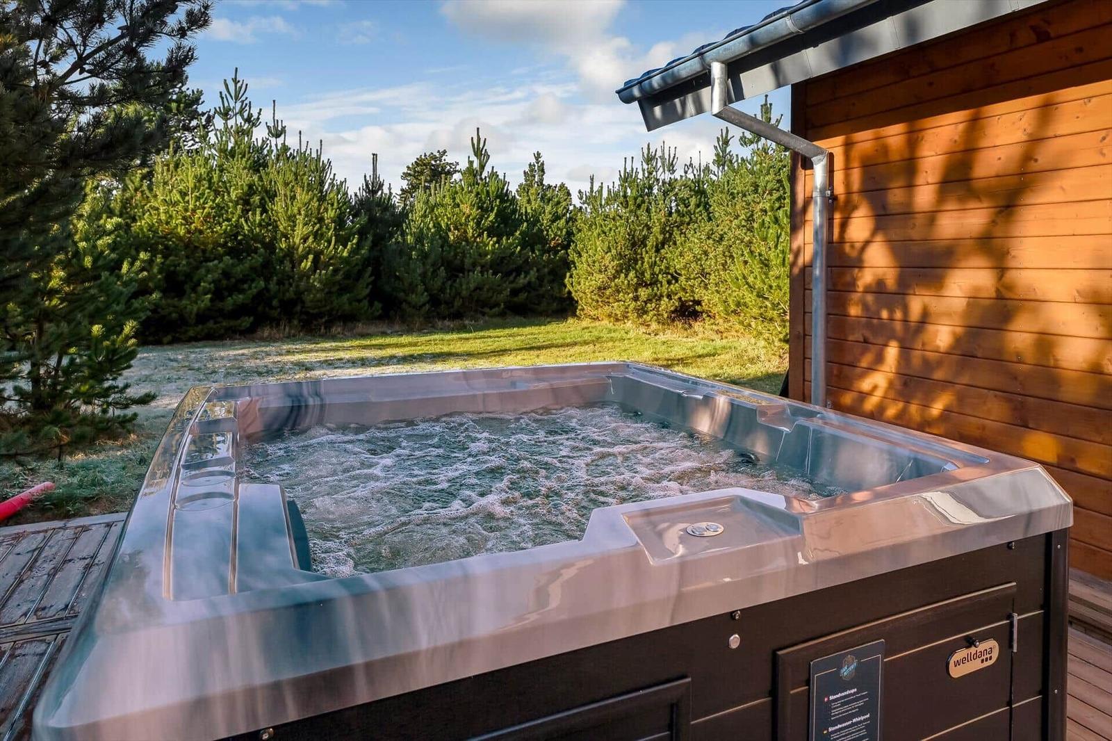 Outdoor hot tub next to wooden house with view of pine trees.
