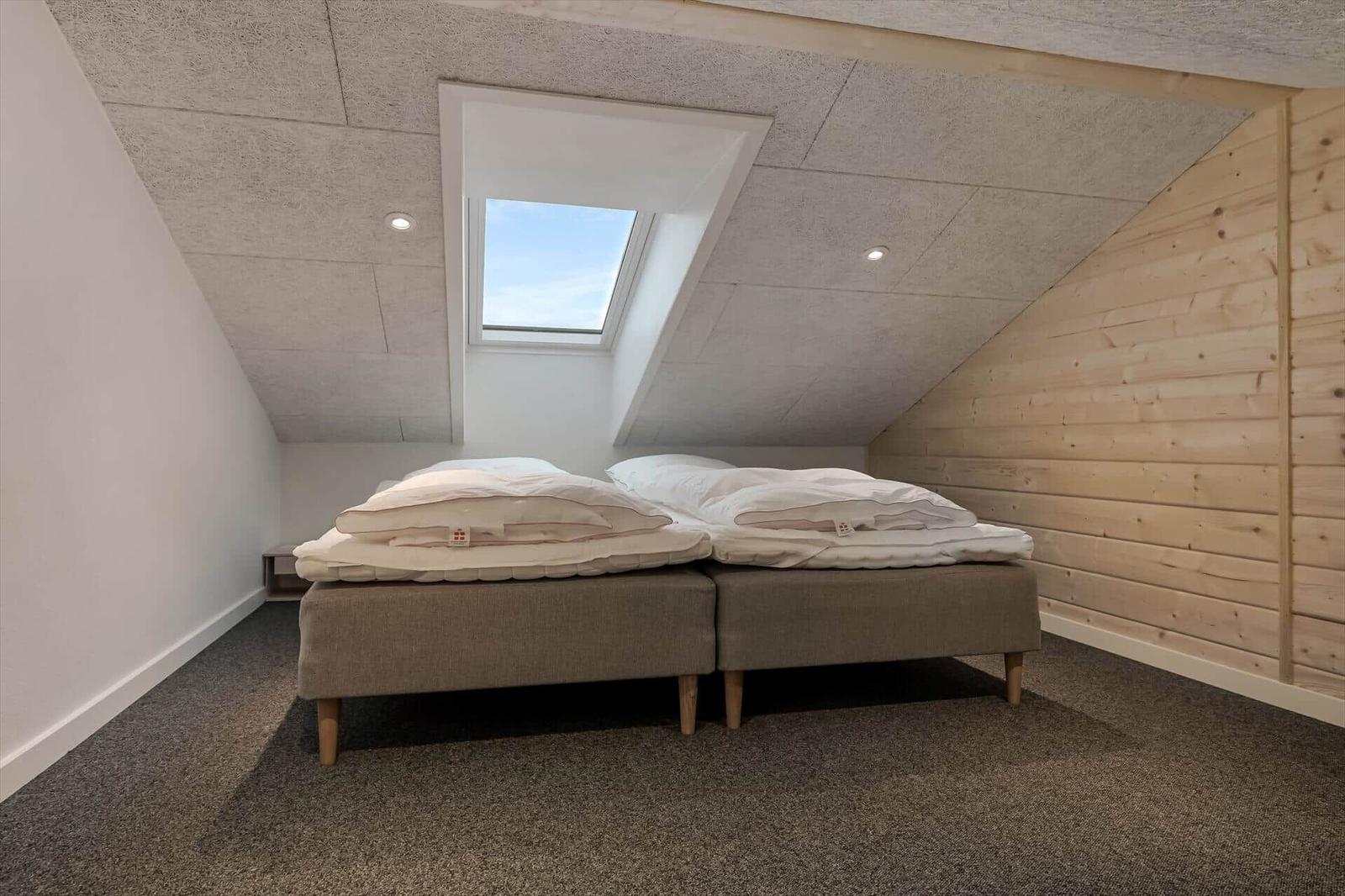 Room with sloped ceiling, double bed, and skylight.