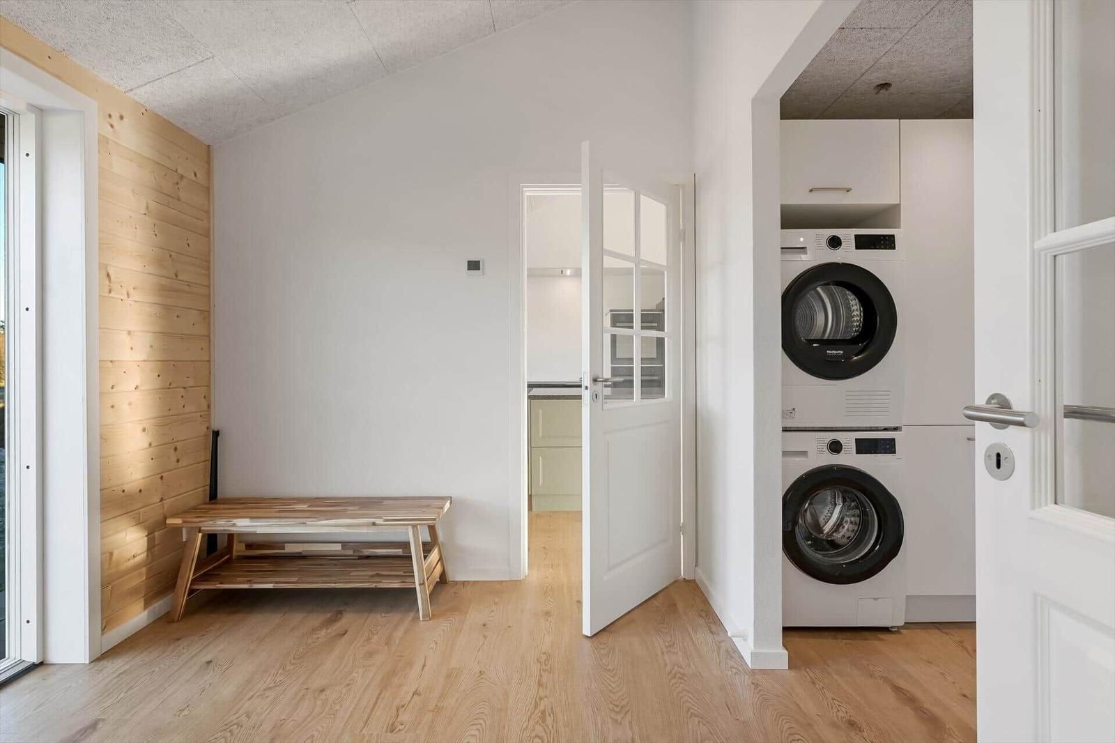 Room with wooden wall, bench, and view into kitchen and laundry
