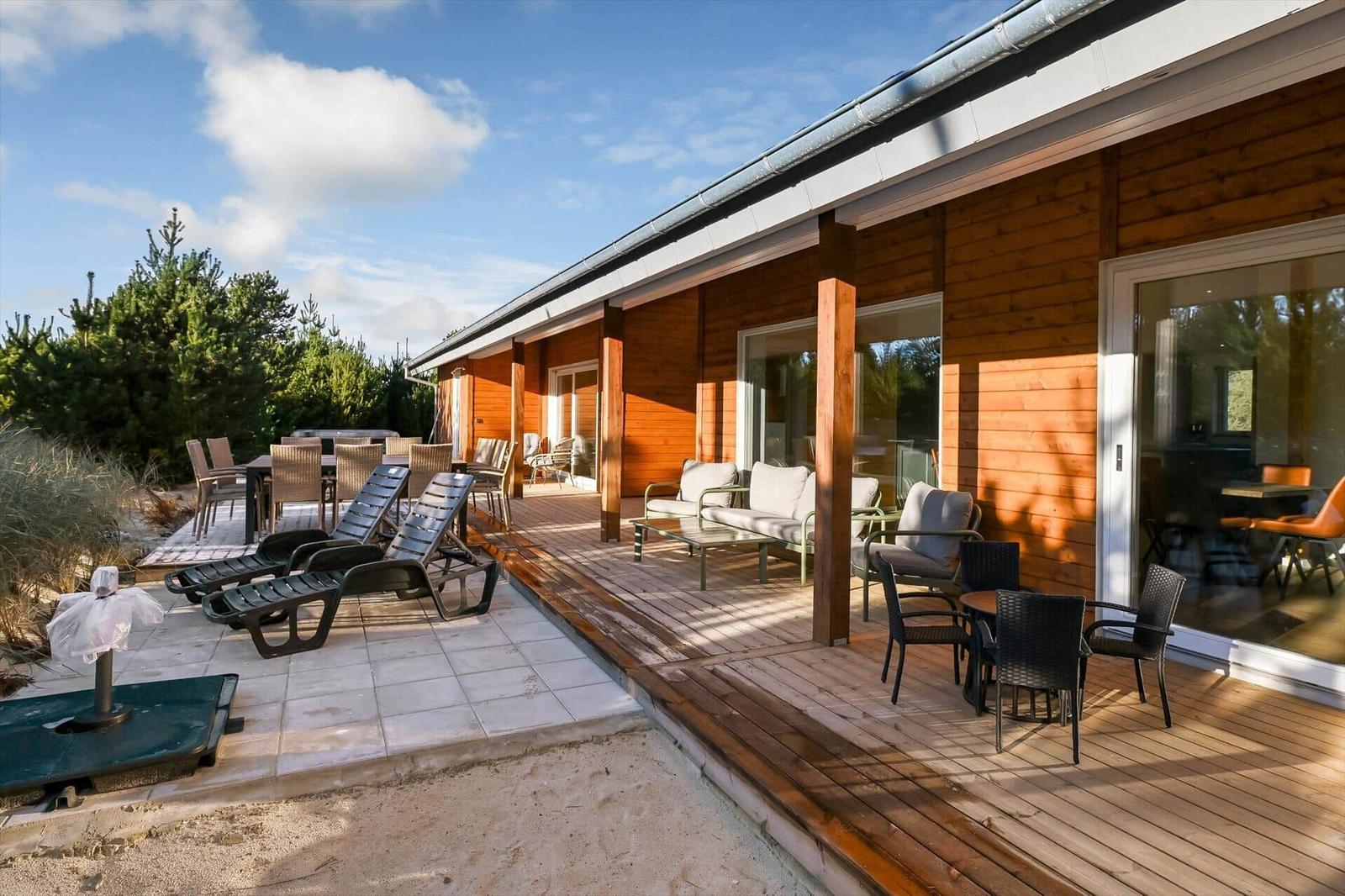 Terrace with lounge area, seating group, and sun loungers beside wooden house with glass front.