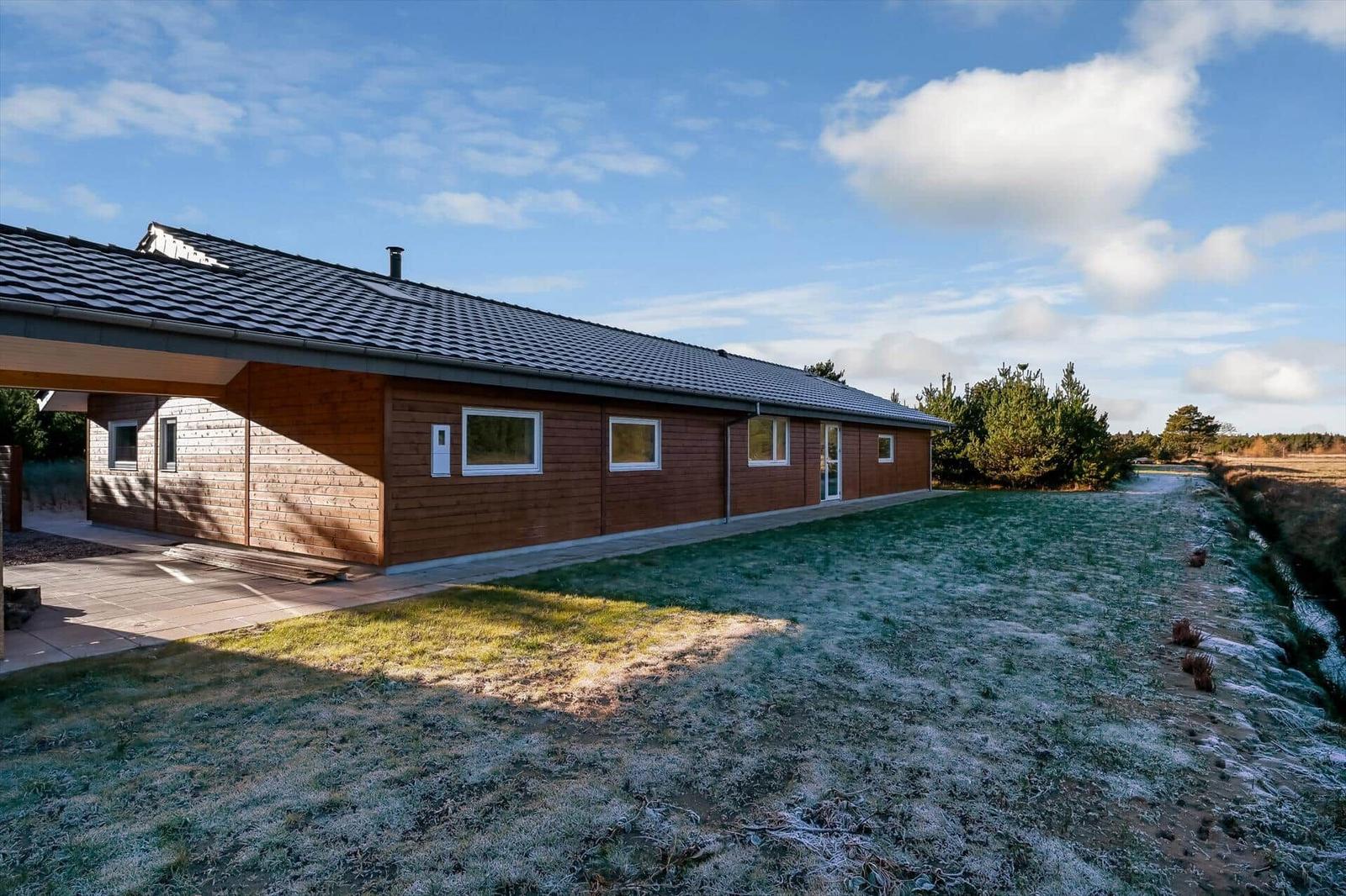 Modern wooden house with frost-covered lawn and view of forest.