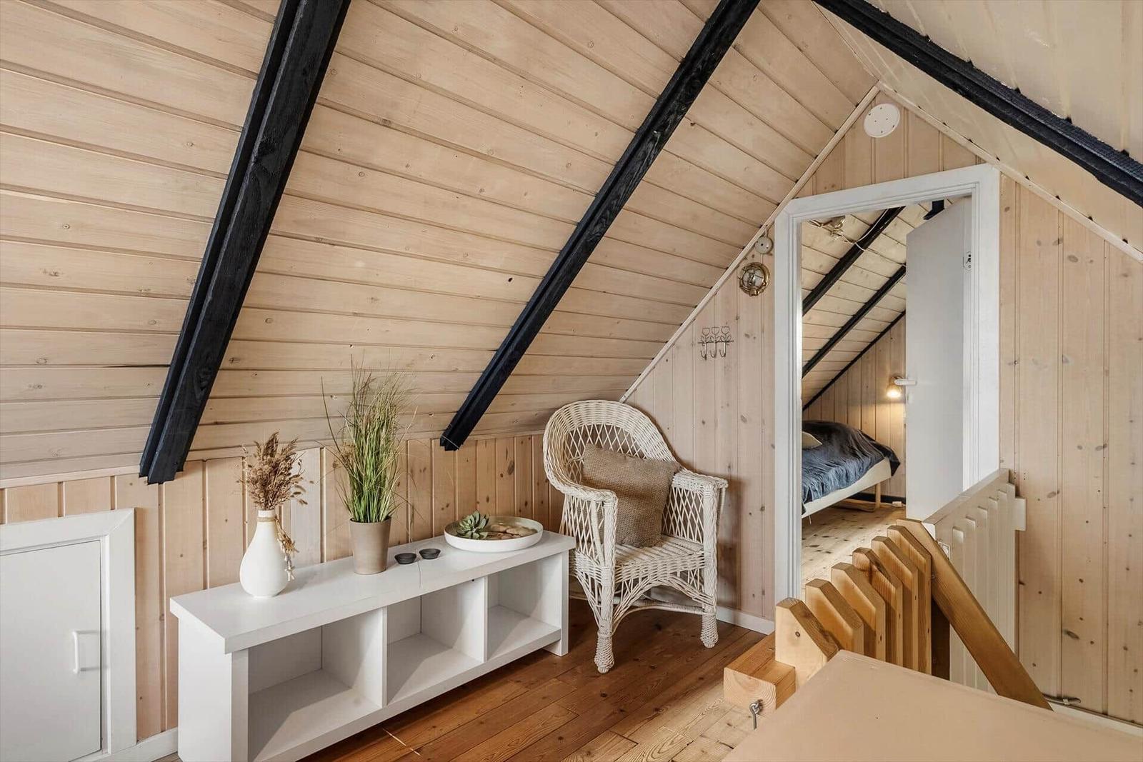 Wohnbereich mit Stuhl und Regal unter Dachschrägen. Treppe führt zu Schlafzimmer.