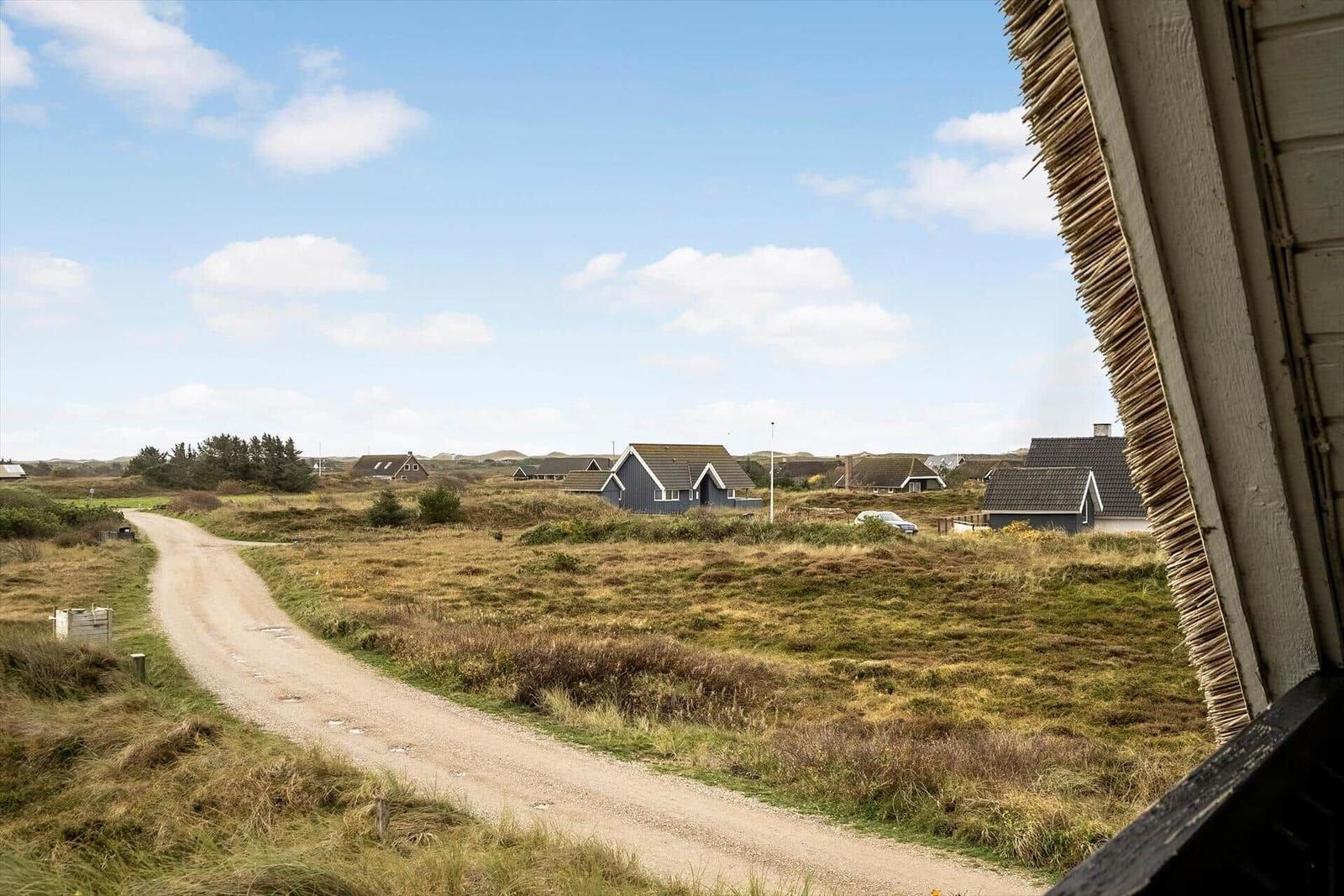 Dorfweg mit Häusern und Grasland unter blauem Himmel