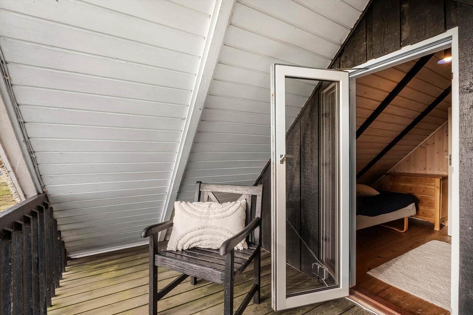 Terrasse mit Stuhl und Blick in Schlafzimmer mit Bett und Holzmöbel.