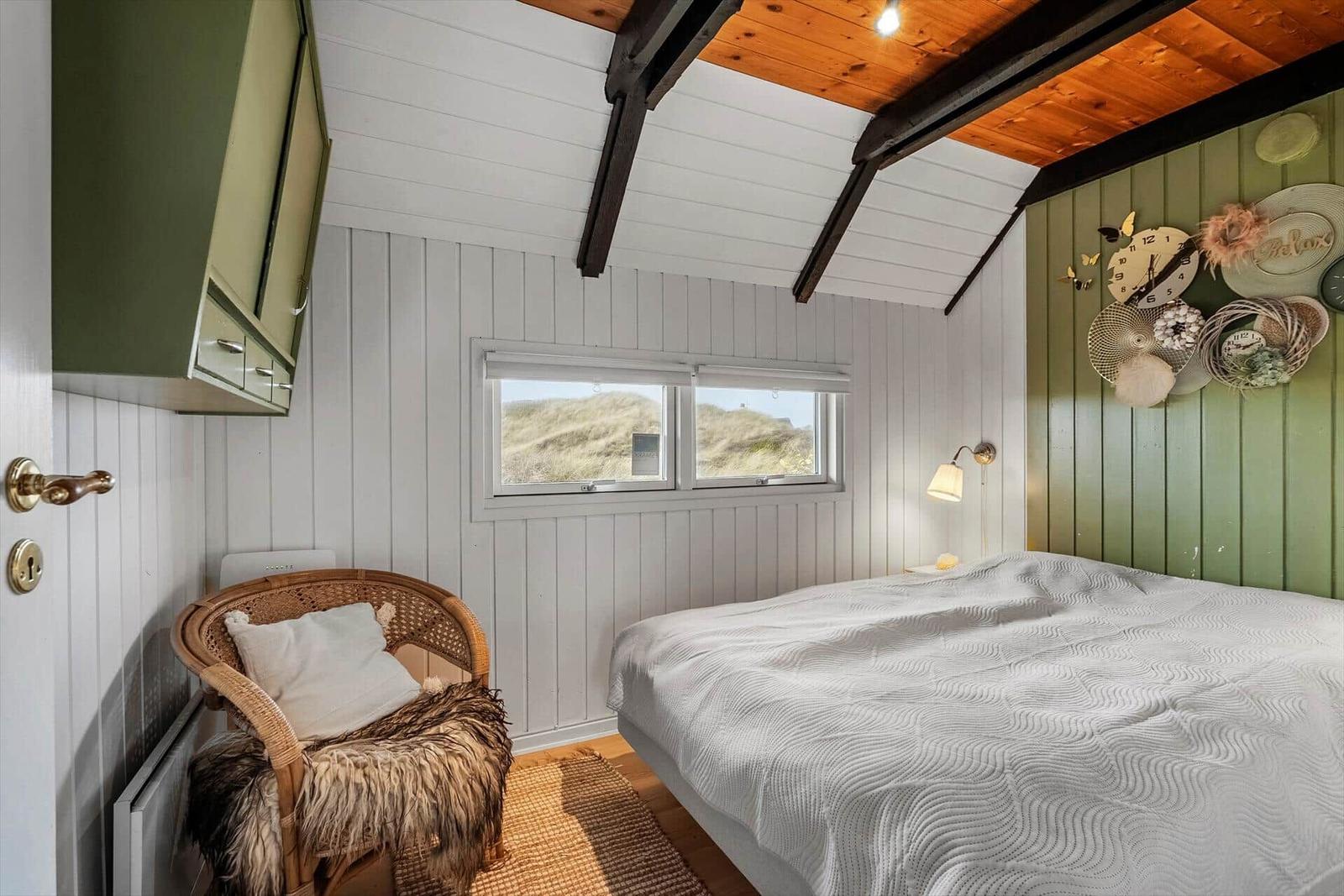 Schlafzimmer mit Bett, Stuhl und Fenster zur Dünenansicht.