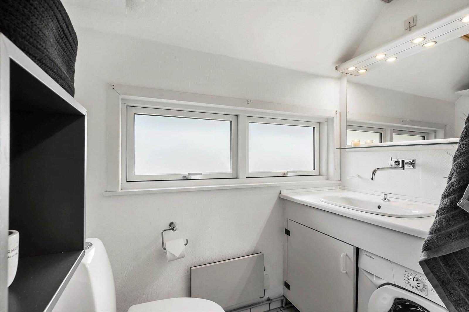 Badezimmer mit Waschmaschine, Spiegel und zwei Fenstern.