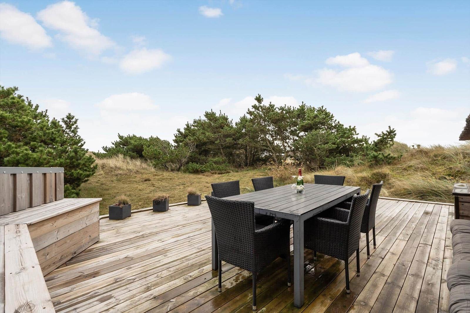 Terrasse mit Esstisch und Stühlen, Blick auf Grünflächen und Bäume.
