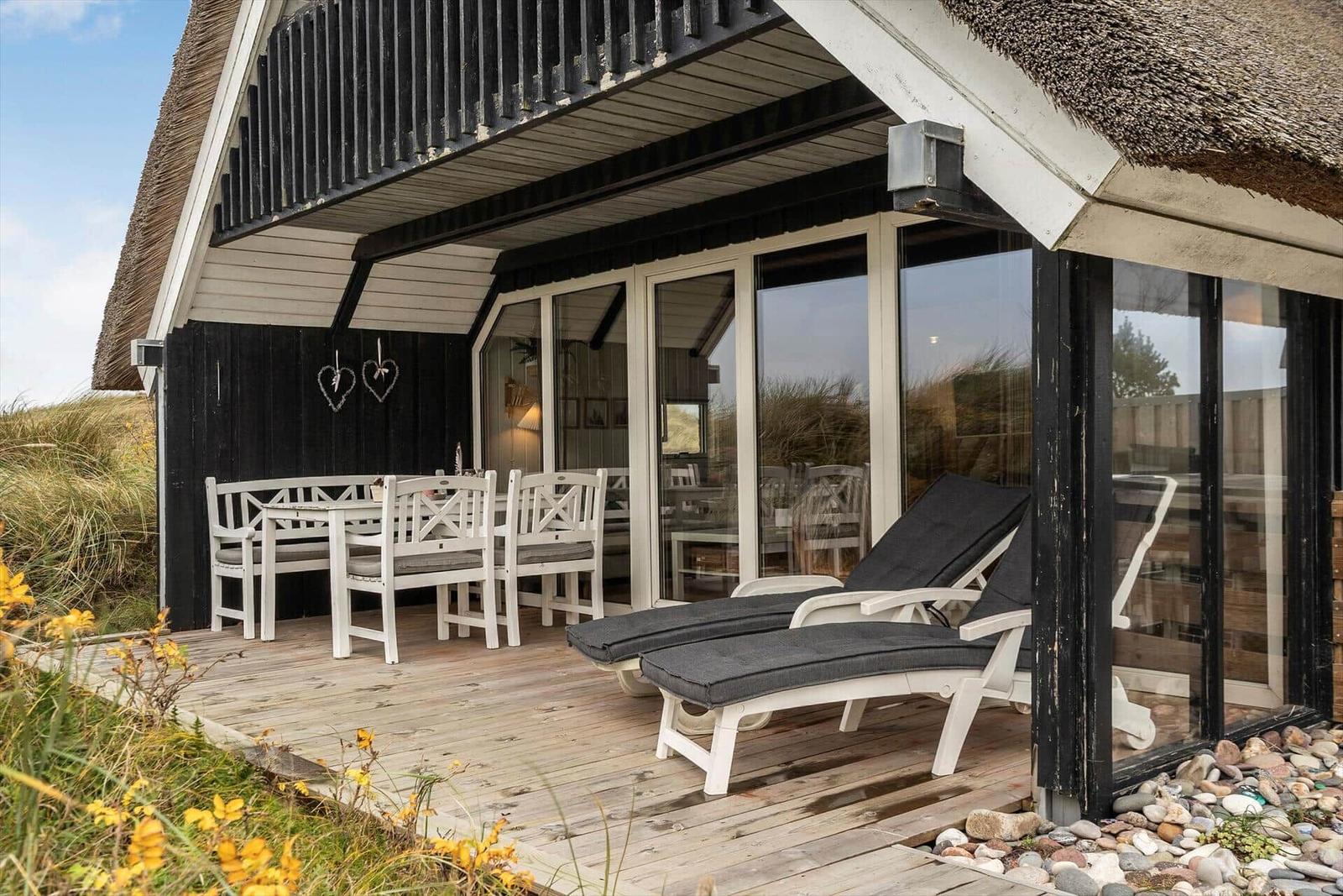 Terrasse mit Tisch, Stühlen und Liegestühlen vor einem Haus mit Strohdach.