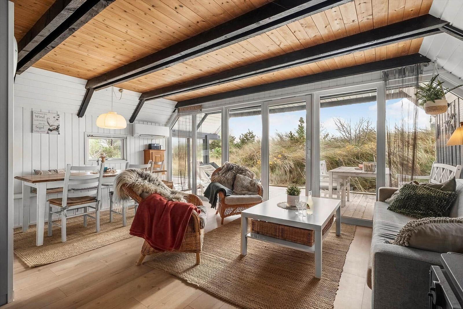 Wohn- und Essbereich mit Holzdecke und großem Fenster zur Terrasse.