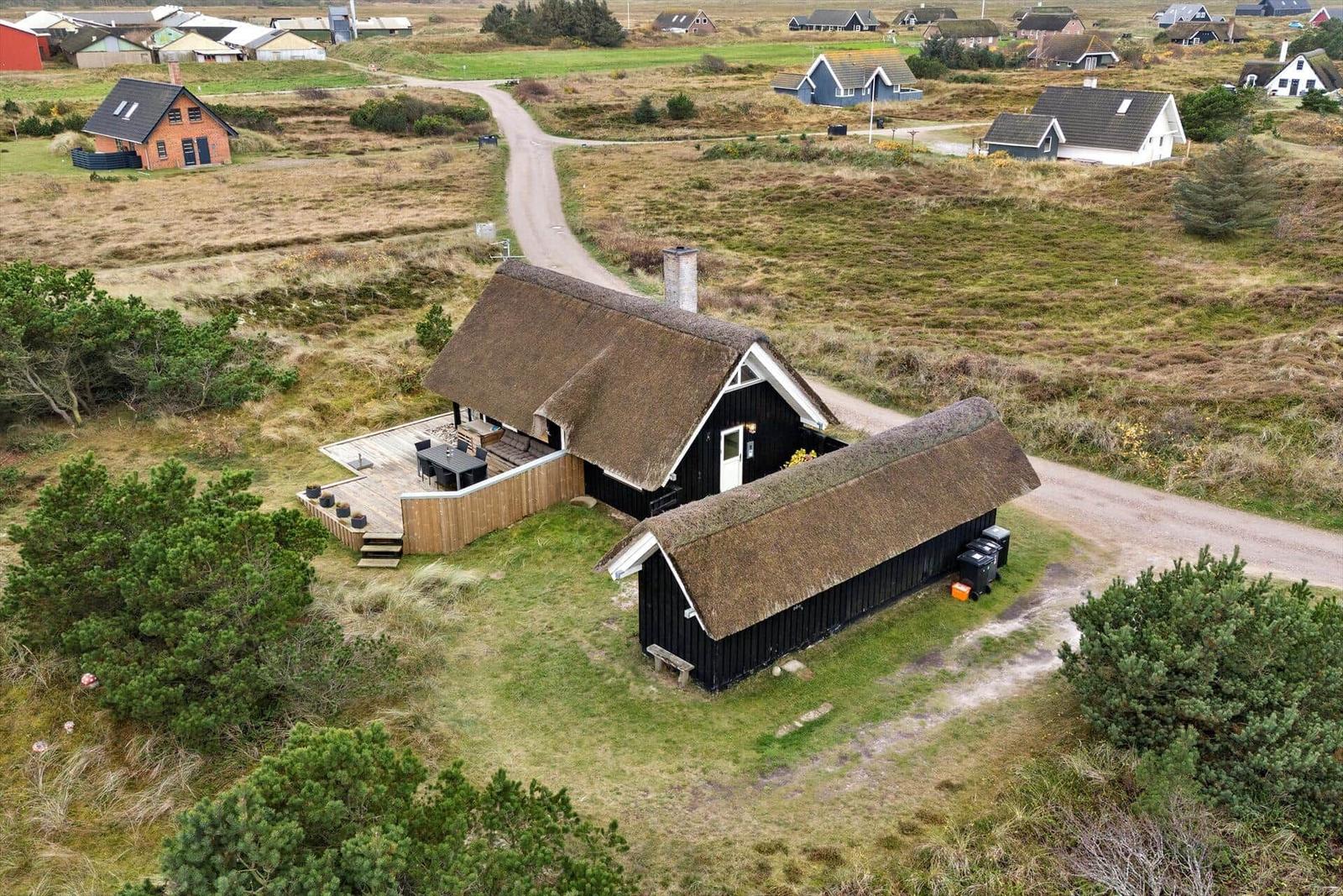 Schwarze Hütte mit Strohdach und Holzterrasse in ländlicher Umgebung.