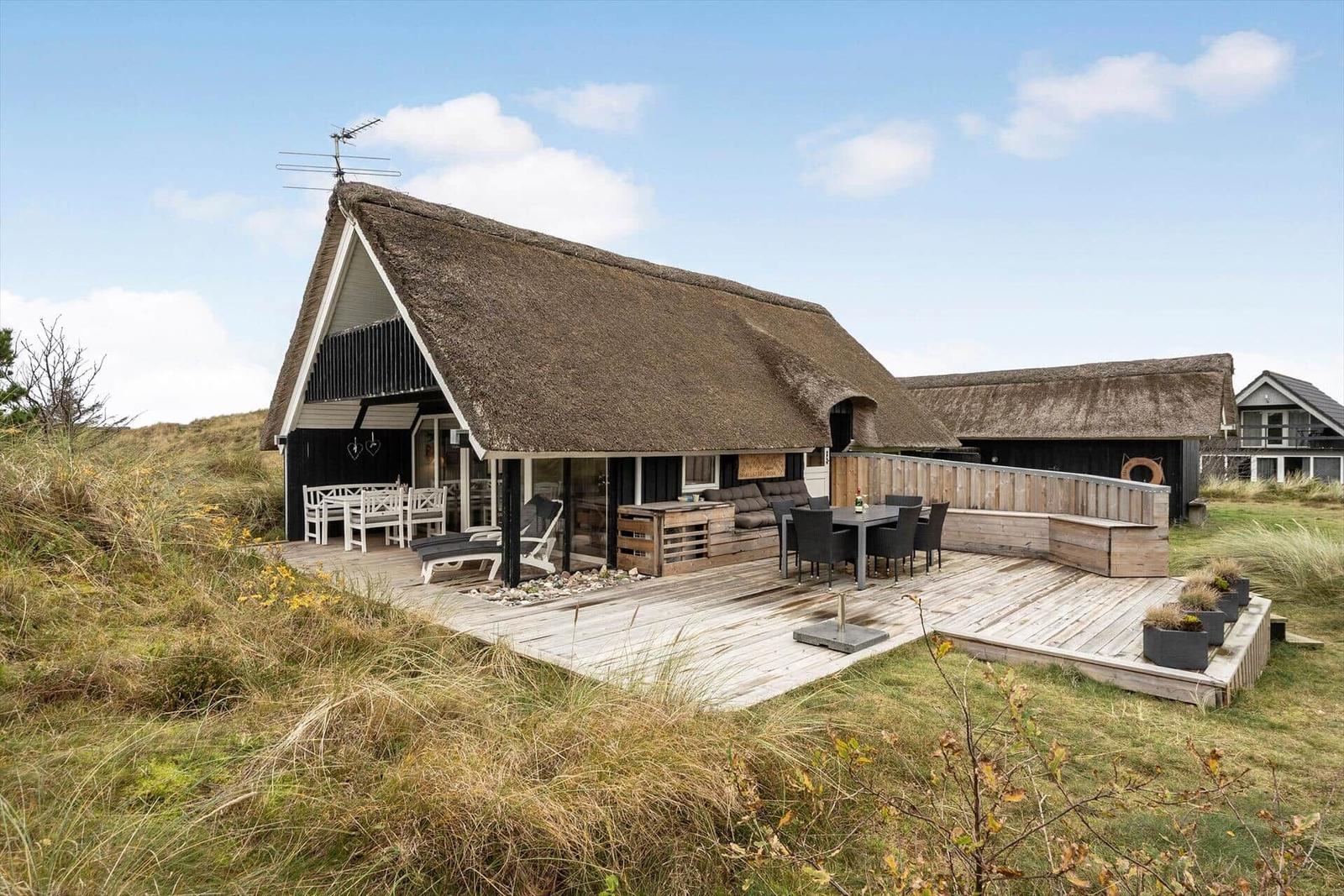 Haus mit Strohdach und großer Terrasse mit Sitzgelegenheiten.