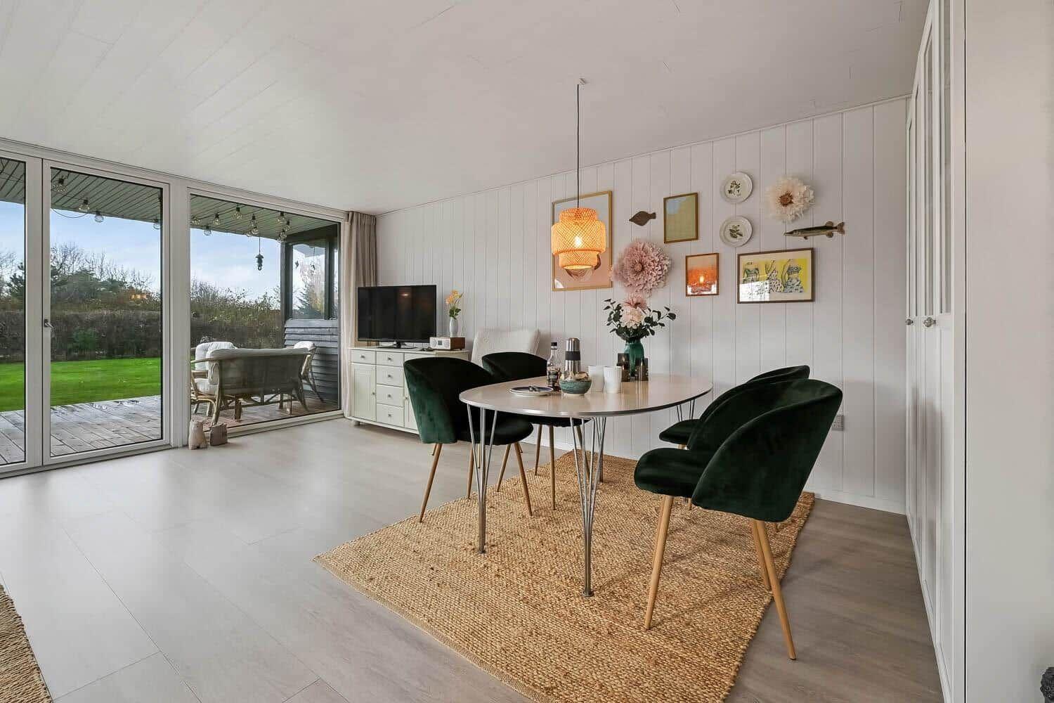 Dining area with green chairs and table on rug. Glass doors lead to terrace with garden.